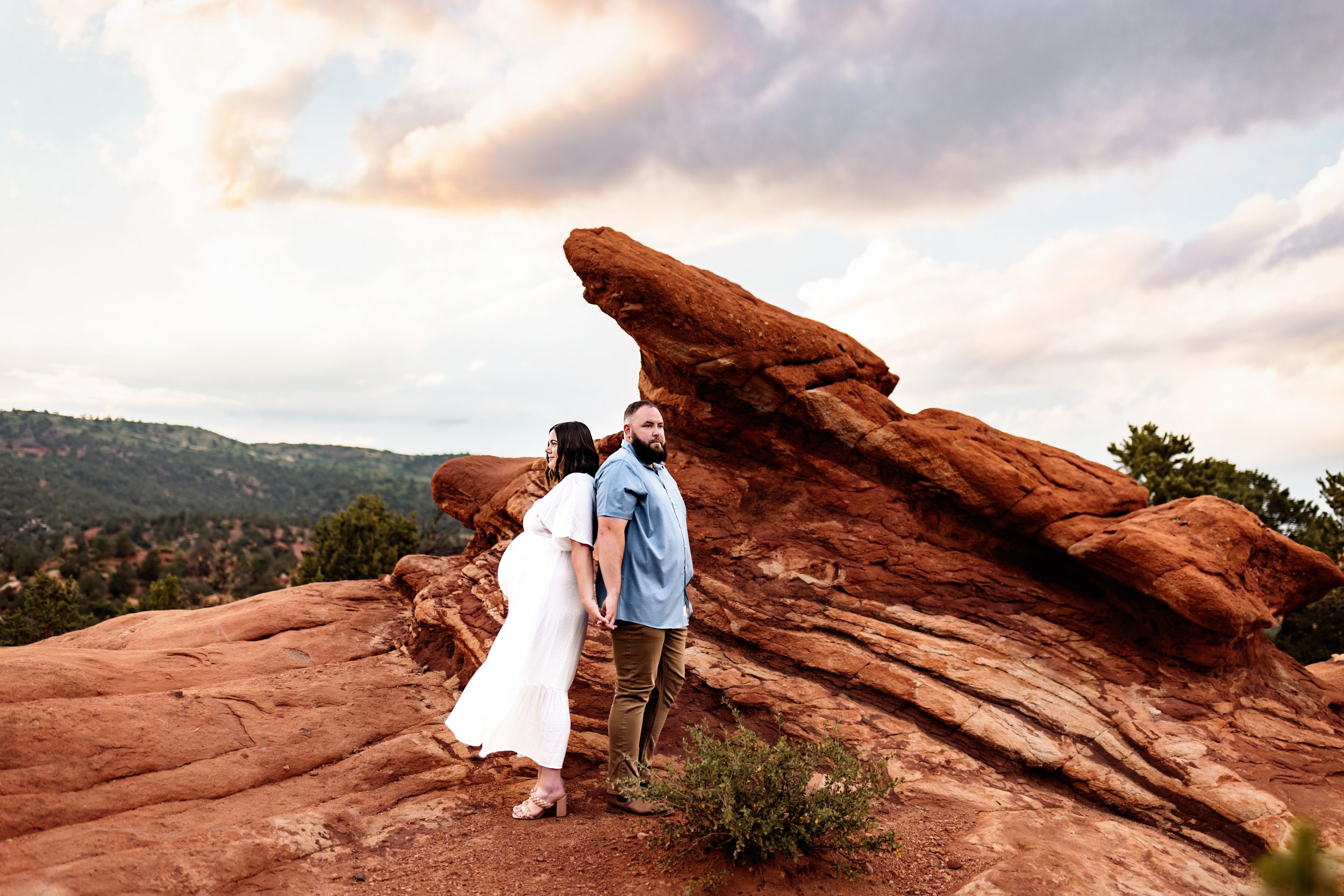 Expecting parents hold hands against a stunning mountain backdrop, highlighting what to wear for maternity photos
