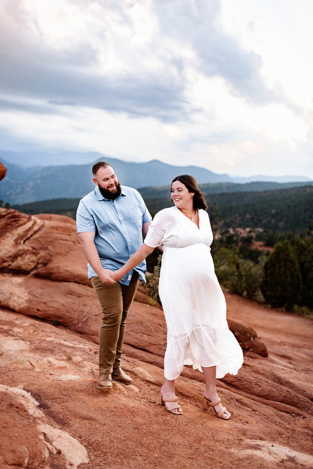 Expecting couple walking hand in hand at Garden of the Gods with scenic mountain views in the background