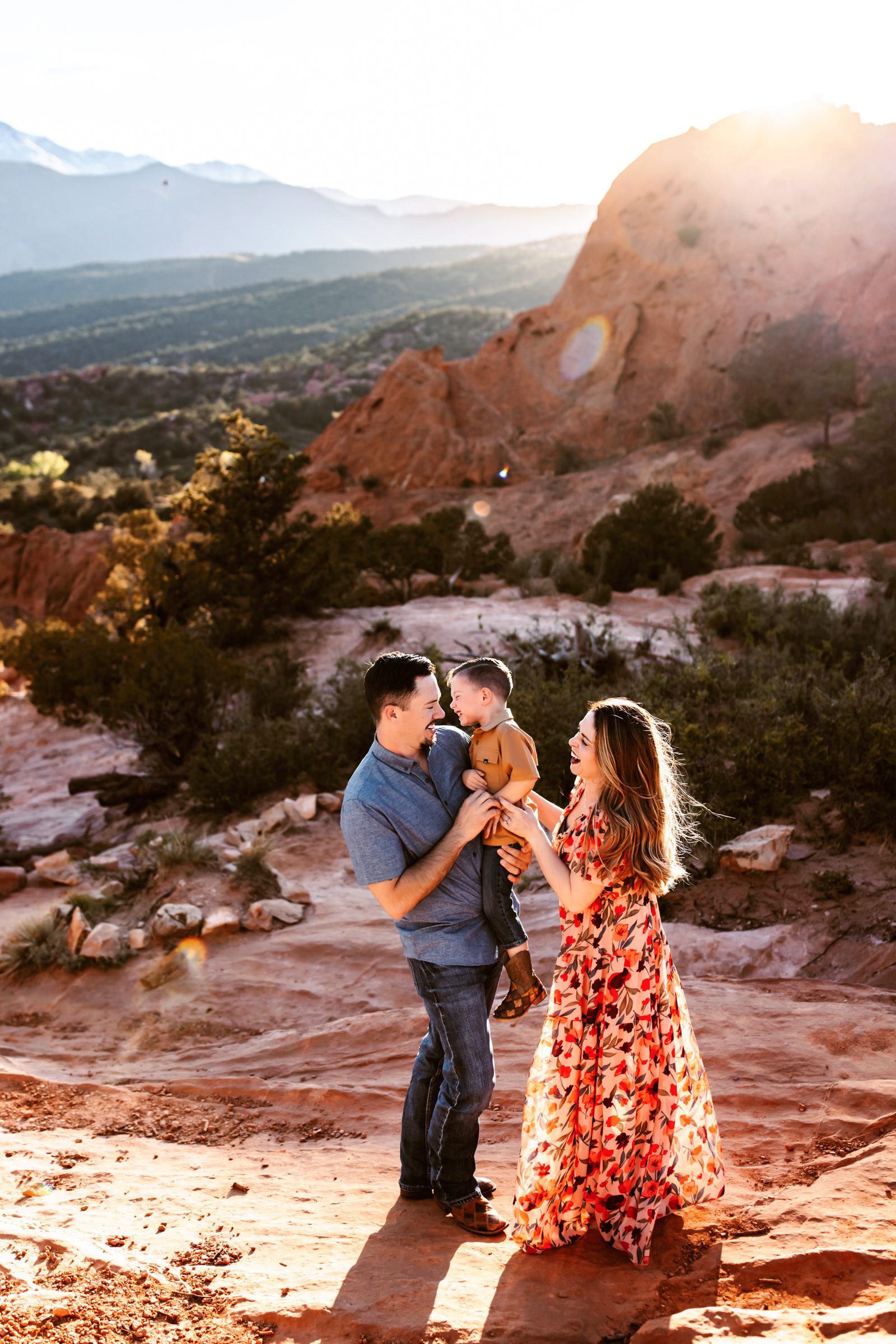 A mother and father laugh with their young son in warm golden light at Garden of the Gods