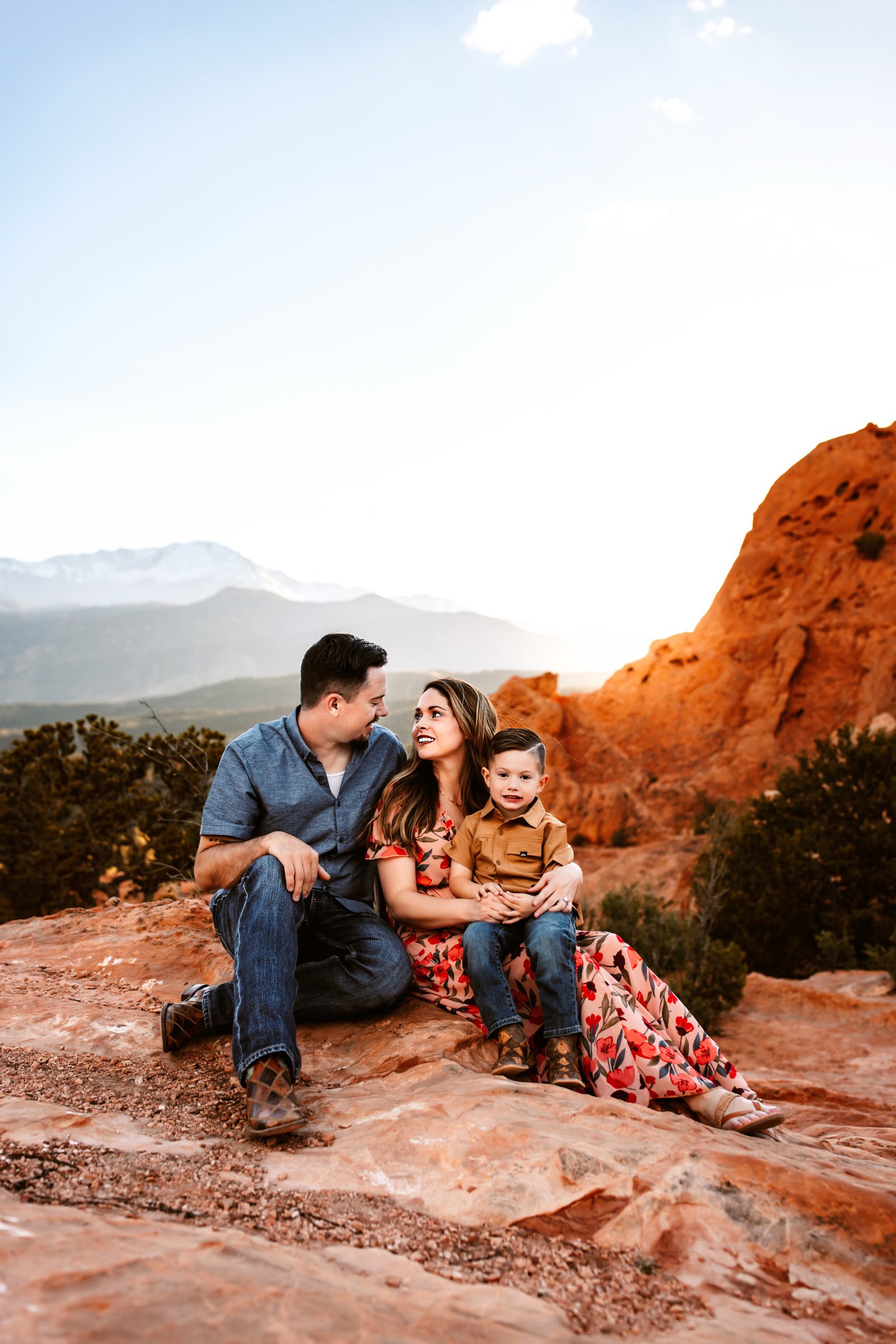 Parents sit on red rocks at Garden of the Gods, sharing a joyful moment with their son during a spring photo session in Colorado Springs.