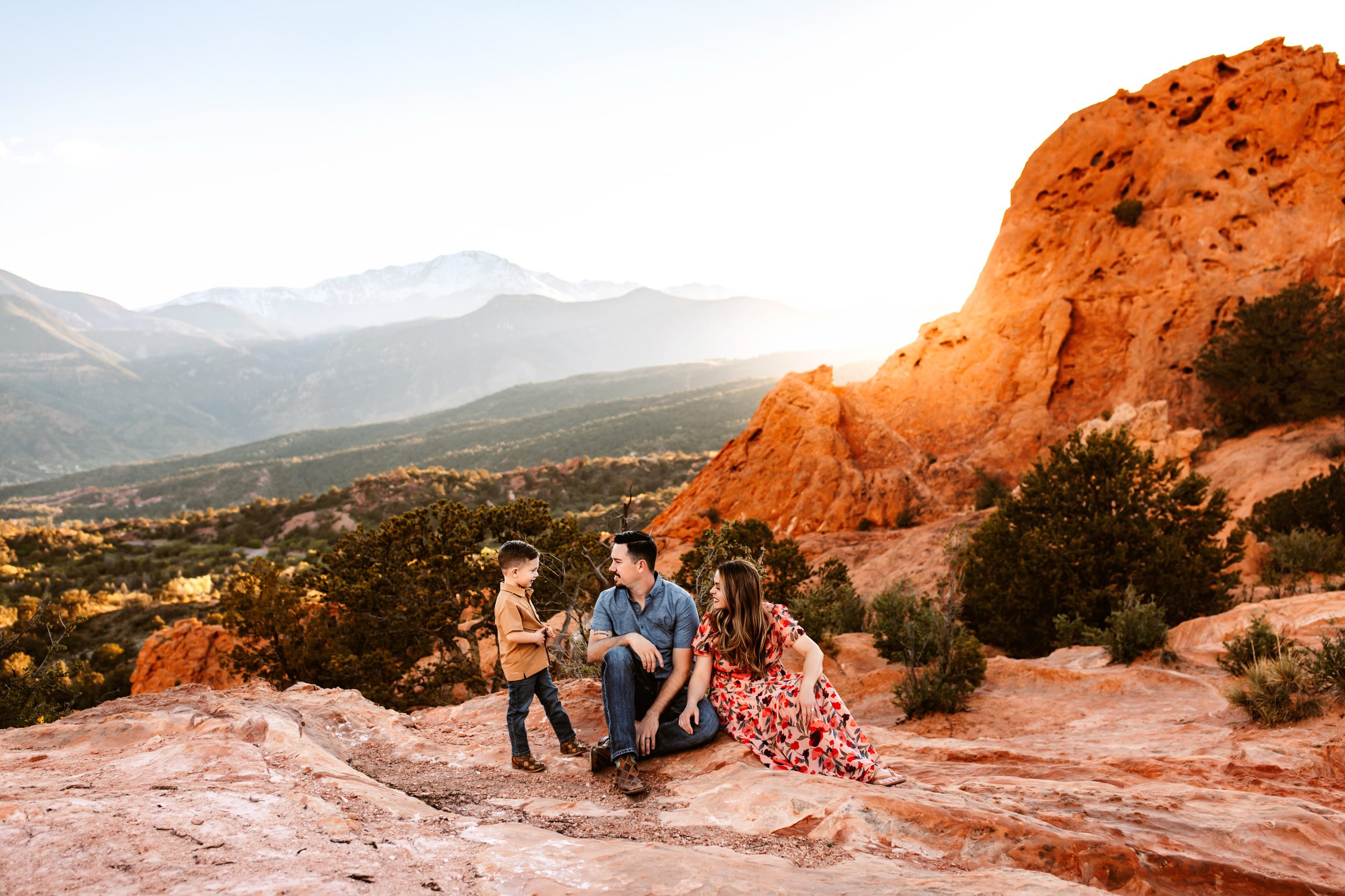 A family sits together on red rock formations with stunning mountain views in the background during their spring photo session in Colorado Springs.