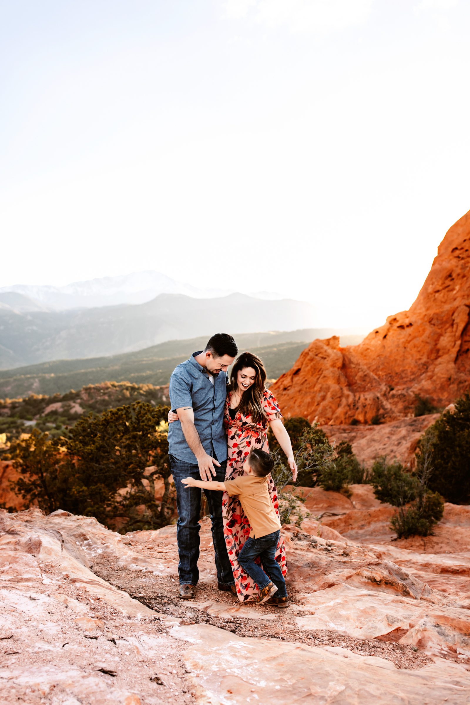 A young boy runs into his parents' arms as they smile at him during a spring photo session in Colorado Springs at sunset.