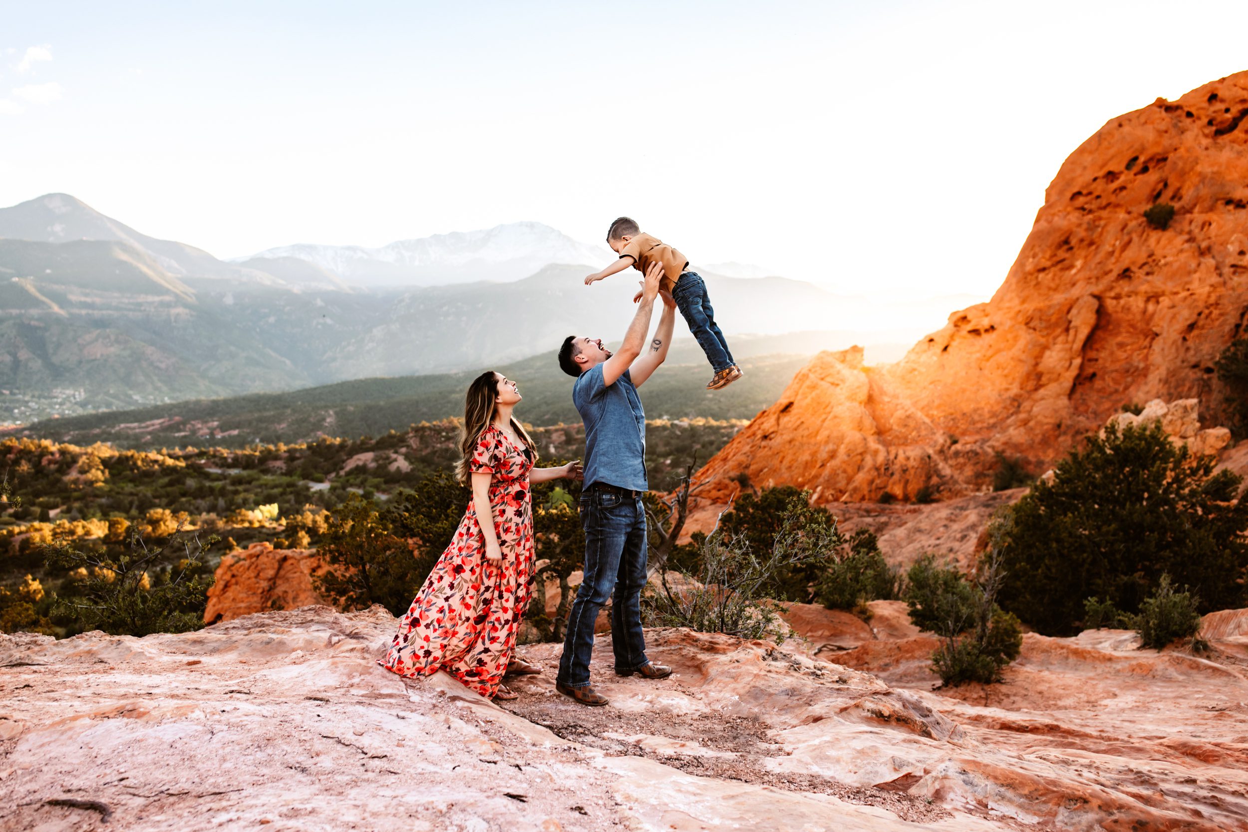 Dad lifting a little boy in the air with a snowy Pikes Peak in the background featuring spring photography sessions in Colorado Springs