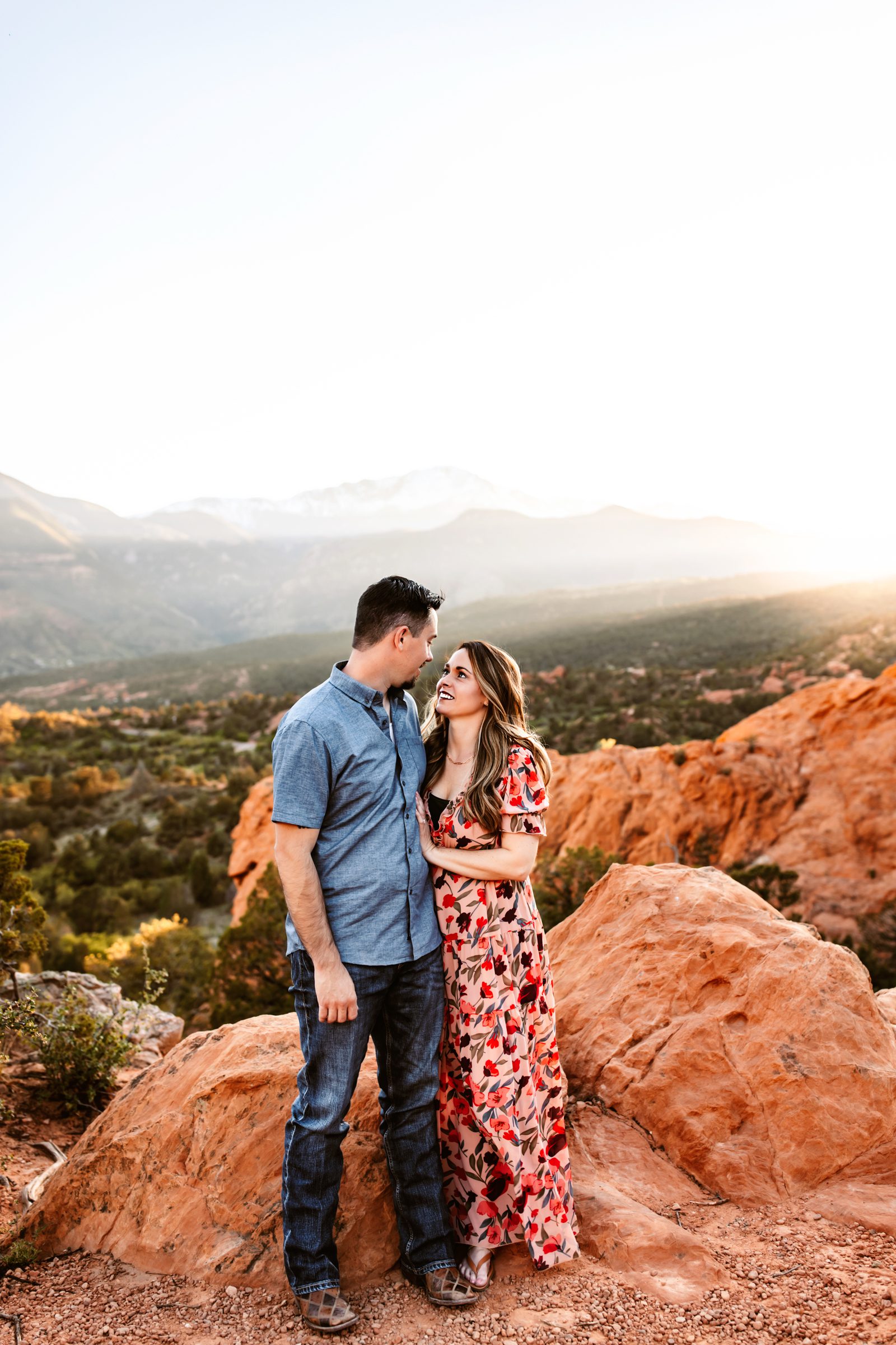A couple shares a loving moment on red rocks with a breathtaking mountain backdrop