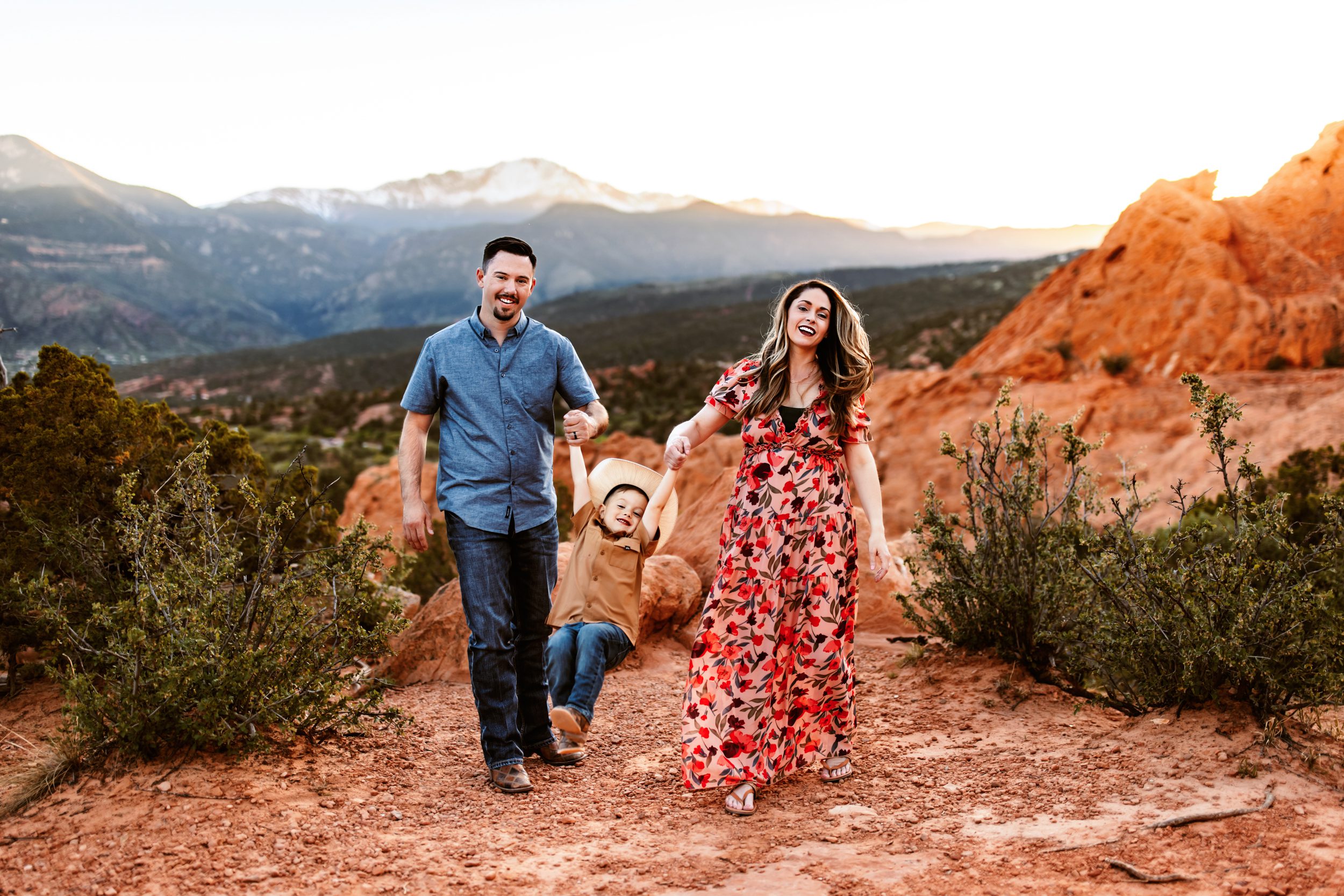 Parents swing their excited child between them as they walk through the red rock landscape, enjoying their spring photo session in Colorado Springs.