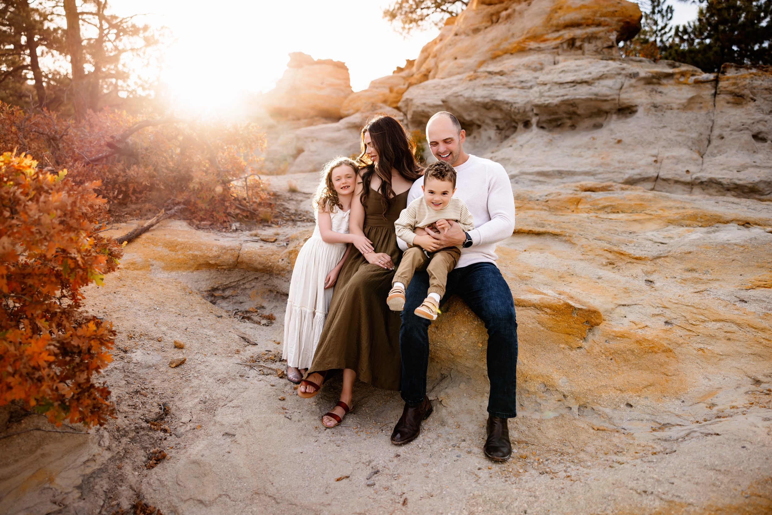 A family sits together on sandstone rocks, laughing and soaking in the golden hues of their Colorado Springs Outdoor Photography Session.