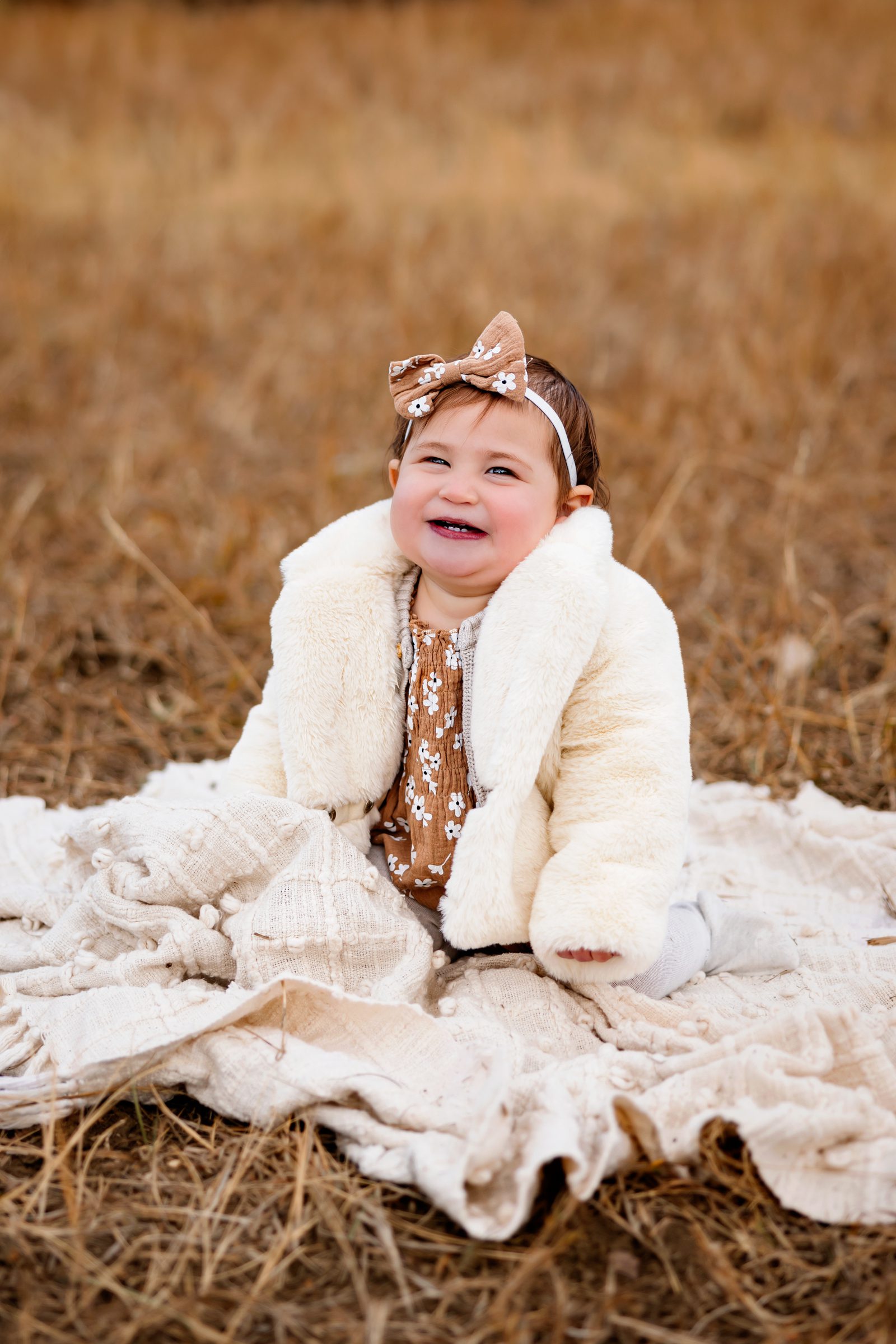A baby girl, dressed in a cozy outfit with a floral bow, flashes a bright smile