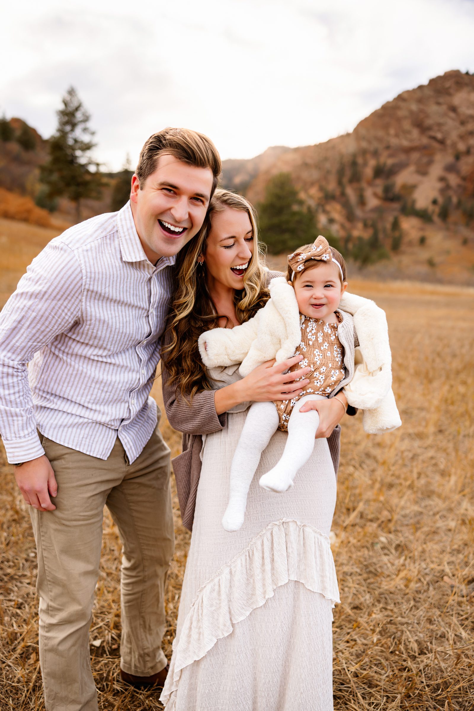 A happy family of three shares laughter in a sunlit field
