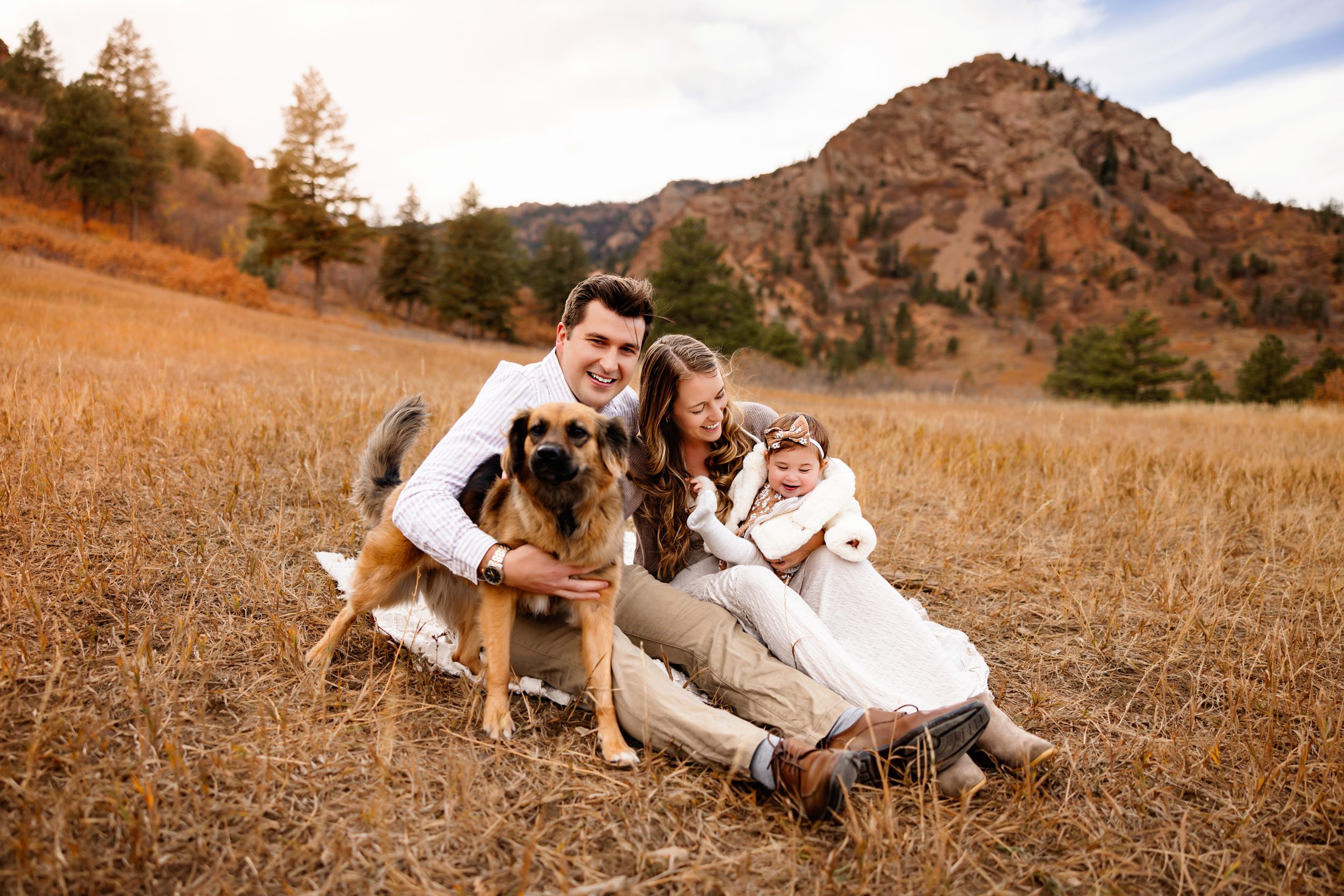 A young family cozies up on a blanket with their beloved dog, enjoying the golden hour glow