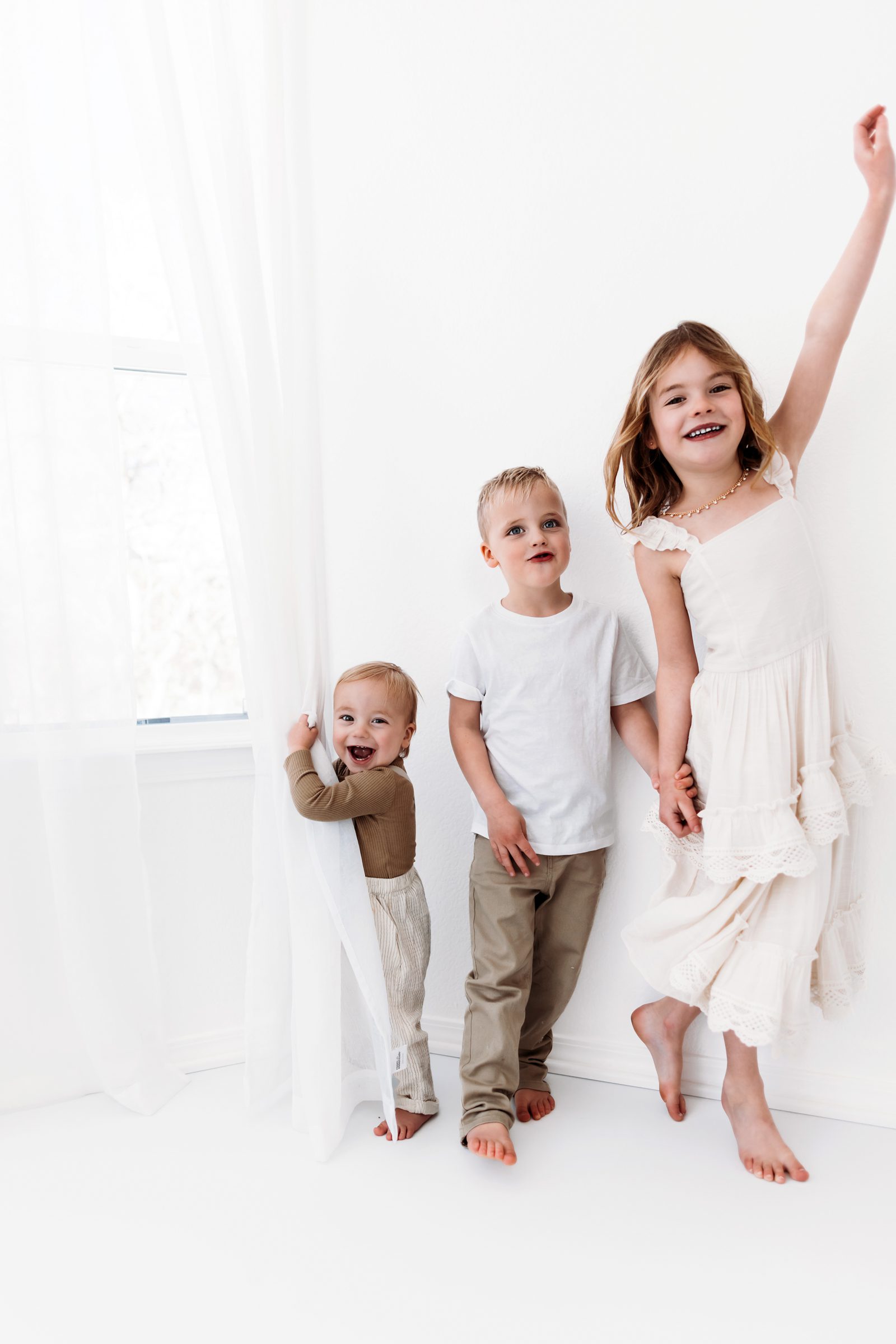 A joyful sibling moment by a white curtain, with the youngest laughing a studio session in Colorado Springs