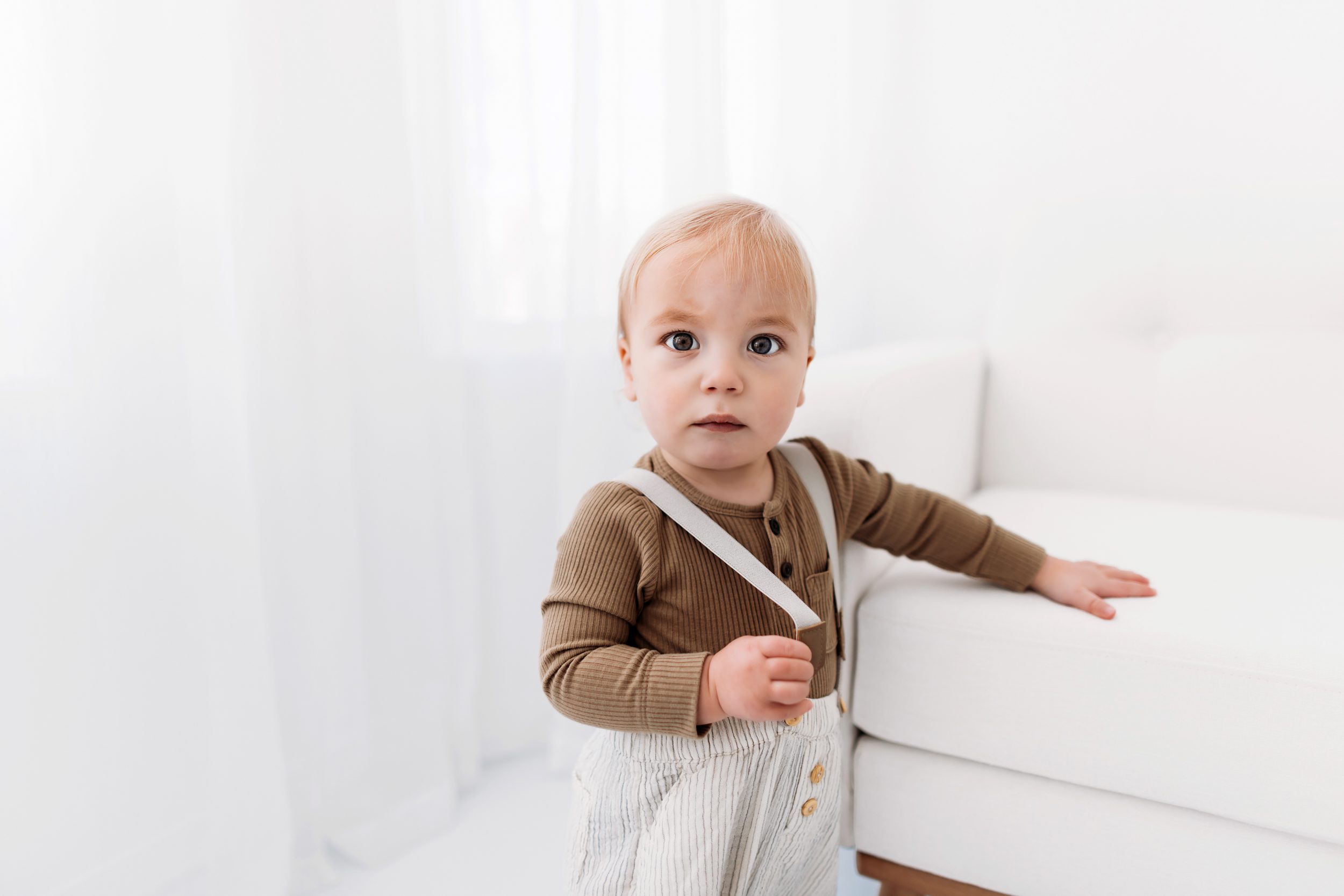 Sibling studio photos in Colorado Springs, featuring a baby standing by a couch.