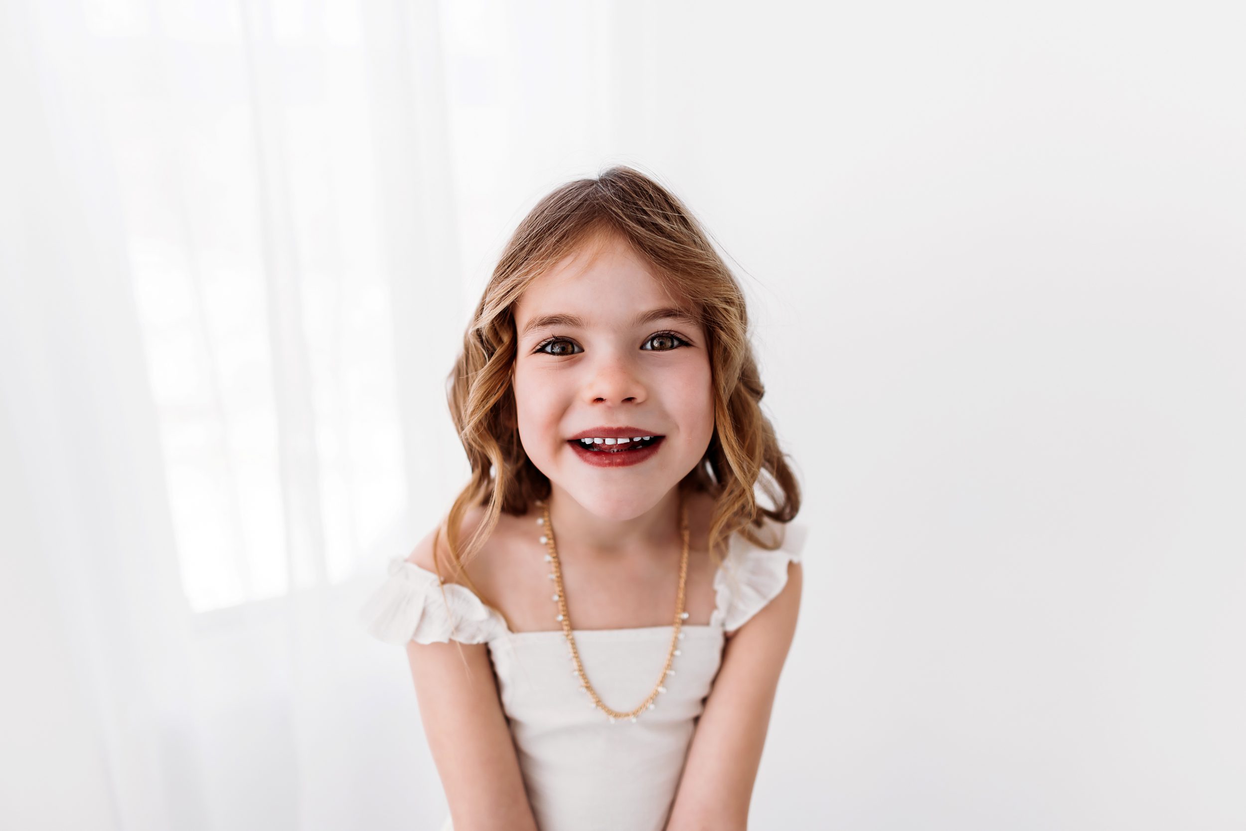 A close-up portrait of a little girl with wavy hair and a beaming smile.