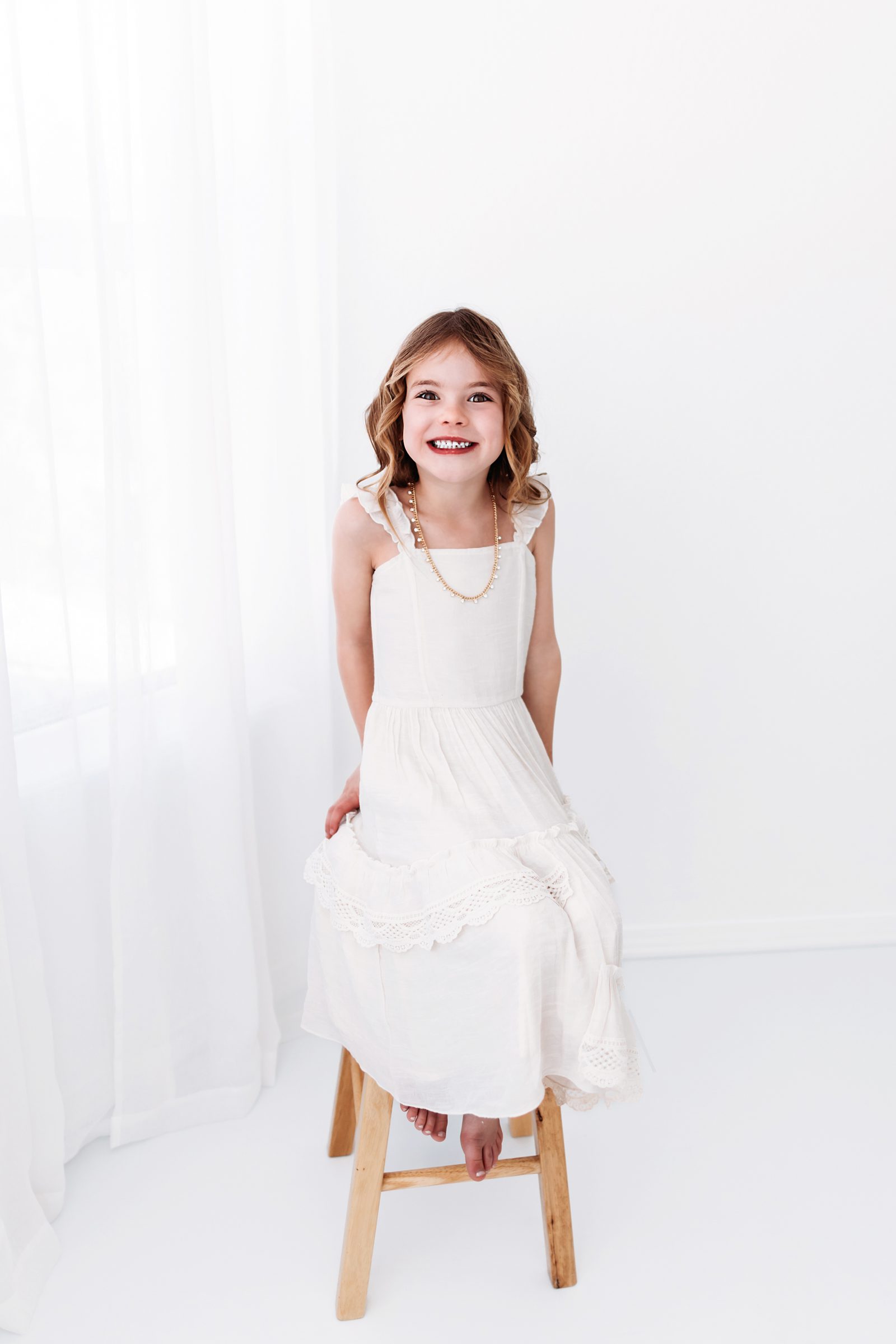 Young girl in a white dress sitting on a wooden stool, smiling