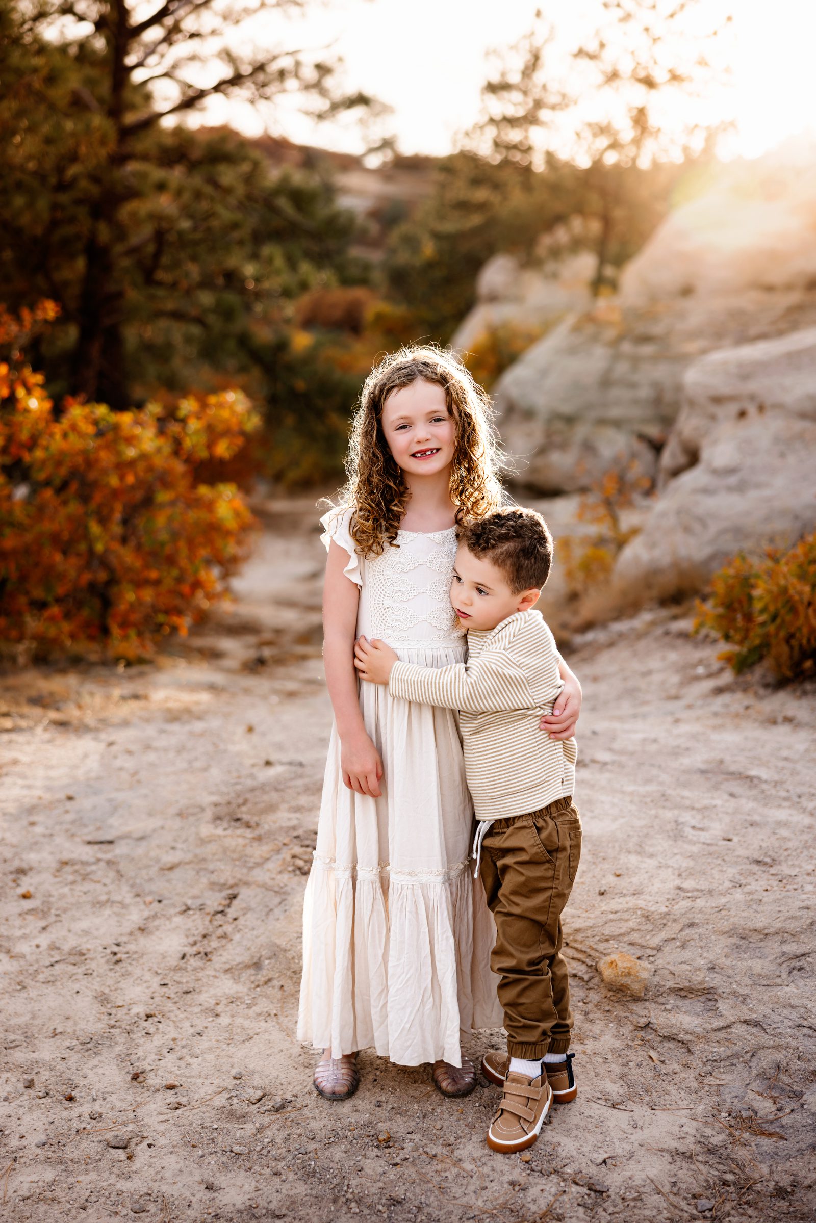 A brother and sister hug tightly, showcasing sibling love amid stunning Colorado landscapes.