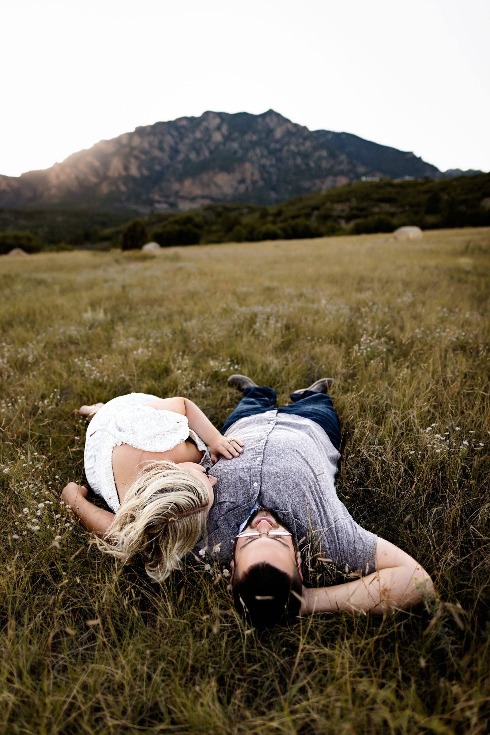 A couple lays in the tall grass under the fading sunlight, enjoying a quiet and intimate moment