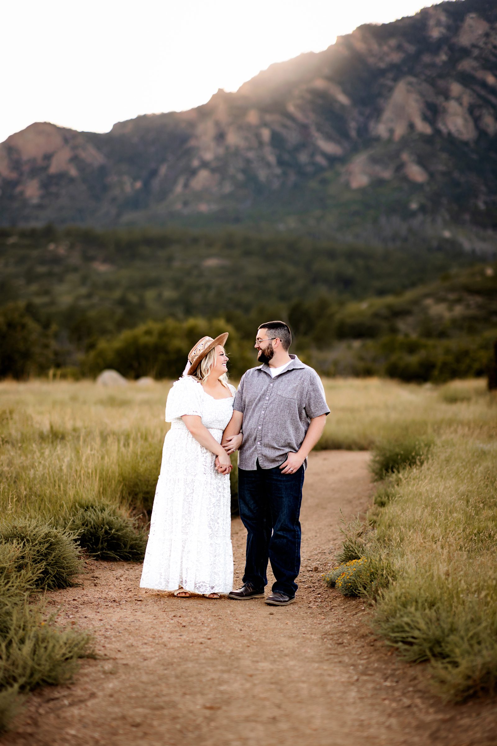 A couple embracing on a scenic dirt path in the mountains bathed in golden evening light.