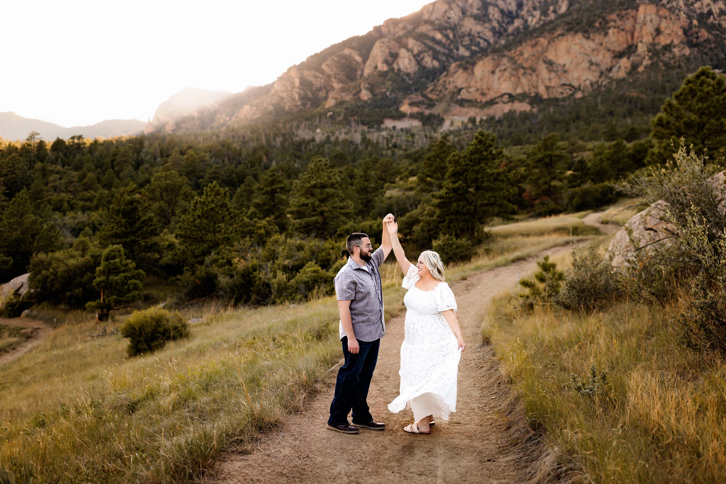 A woman in a flowing white dress holds her partner’s hand while twirling on a dirt path, capturing a dreamy and romantic moment