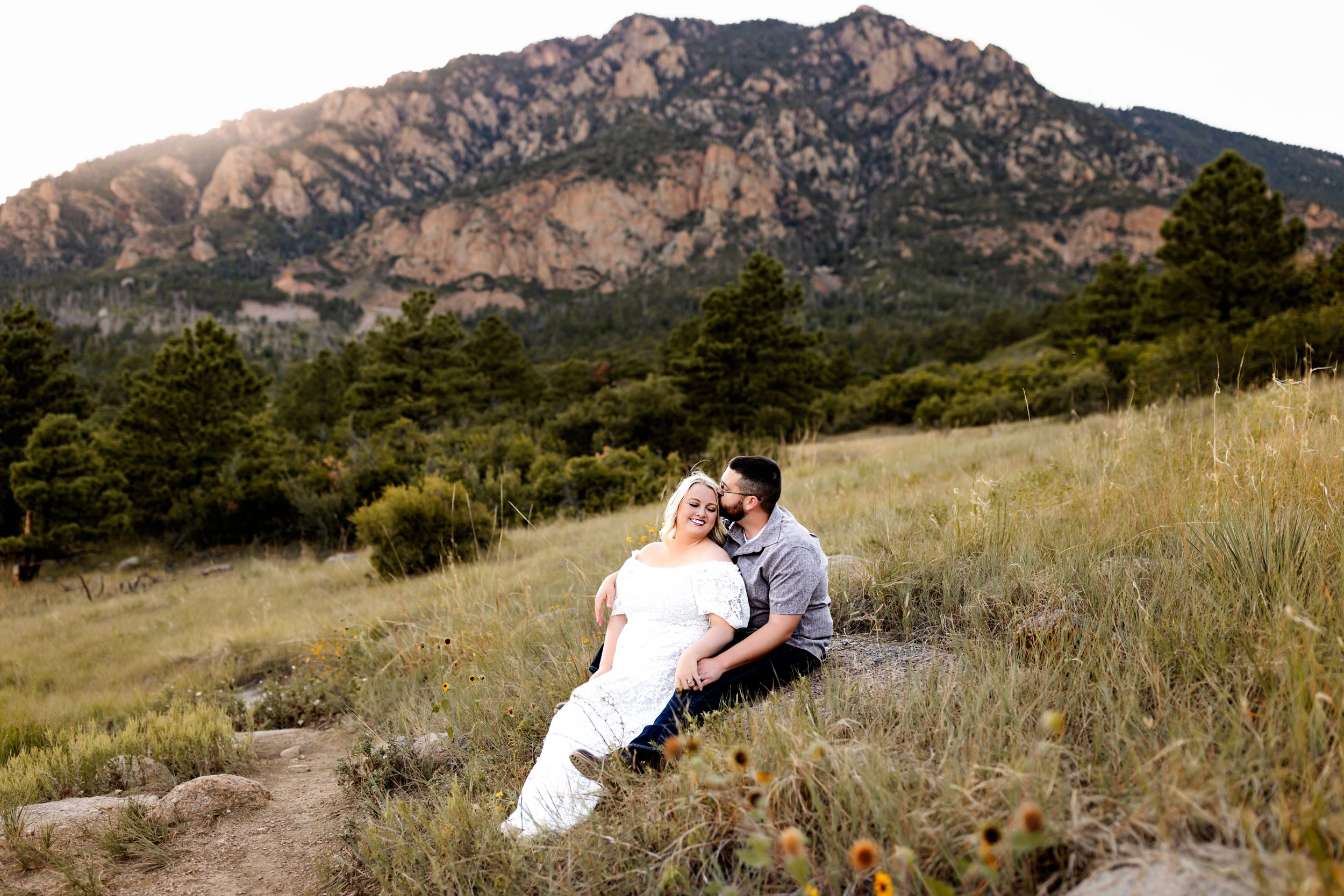 A couple sharing laughter as they sit on a rock in the middle of a scenic meadow, soaking in the beauty