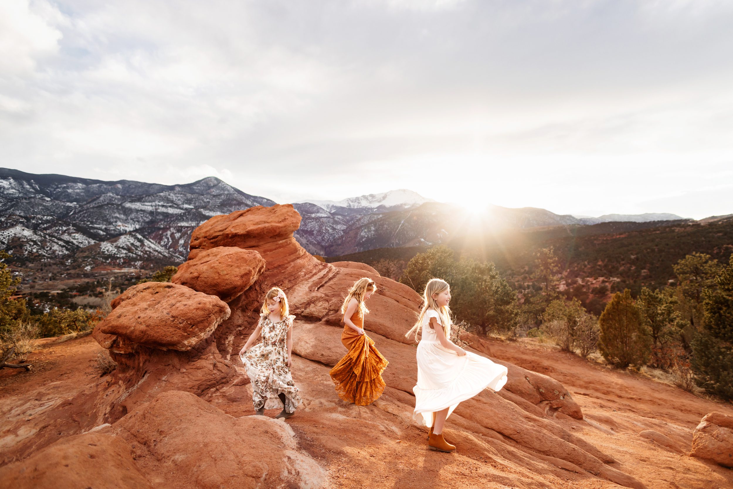 Three girls twirling joyfully on the red rocks as the sun sets behind them