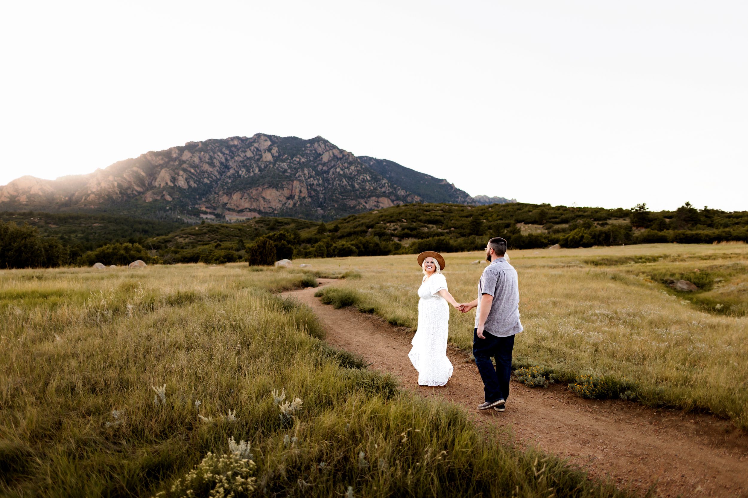 Anniversary Photos in Colorado Springs of a woman turning back with a big smile while holding hands with her partner on a winding mountain path