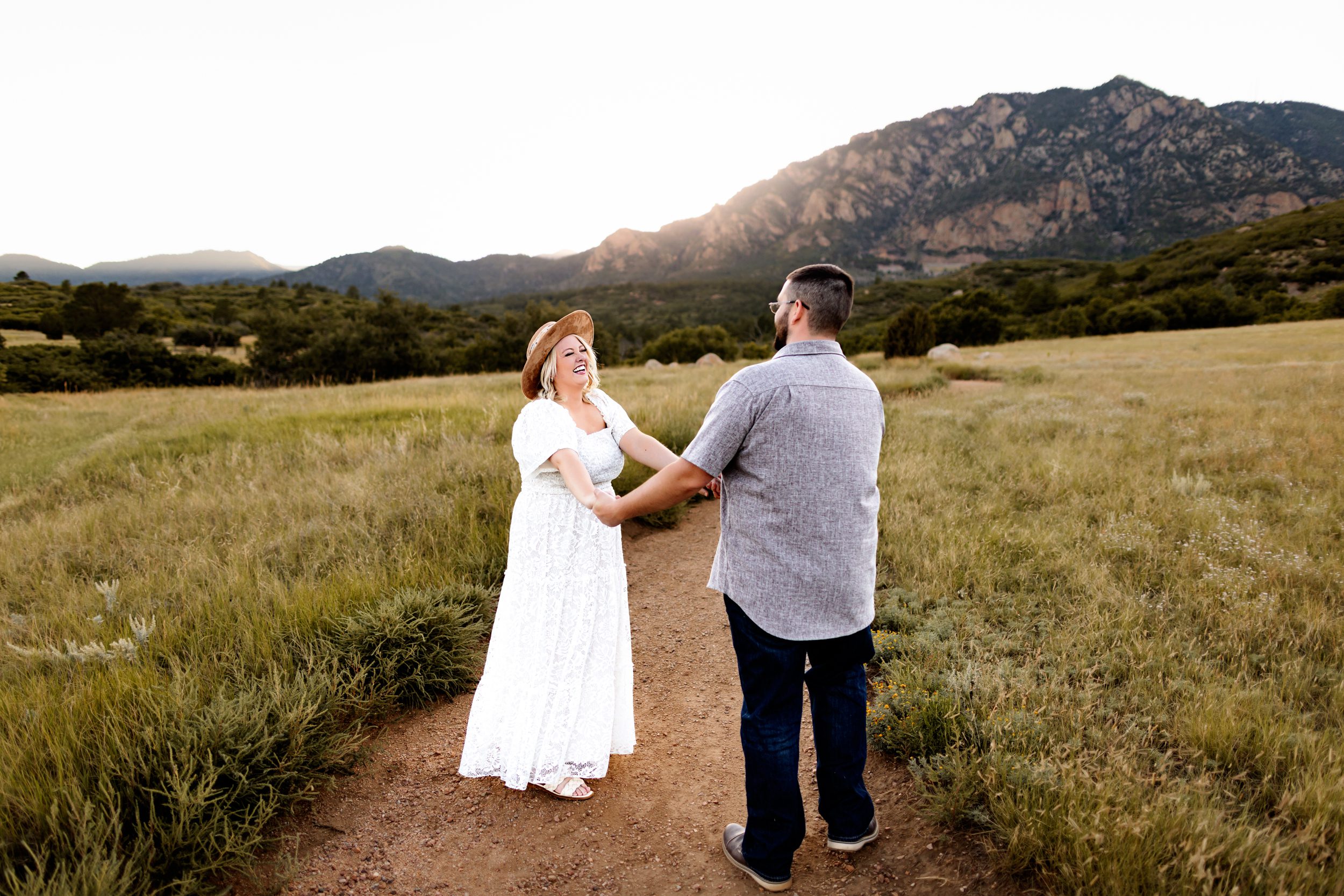 A joyful moment between a couple holding hands and laughing while standing in the middle of a path lined with green grass