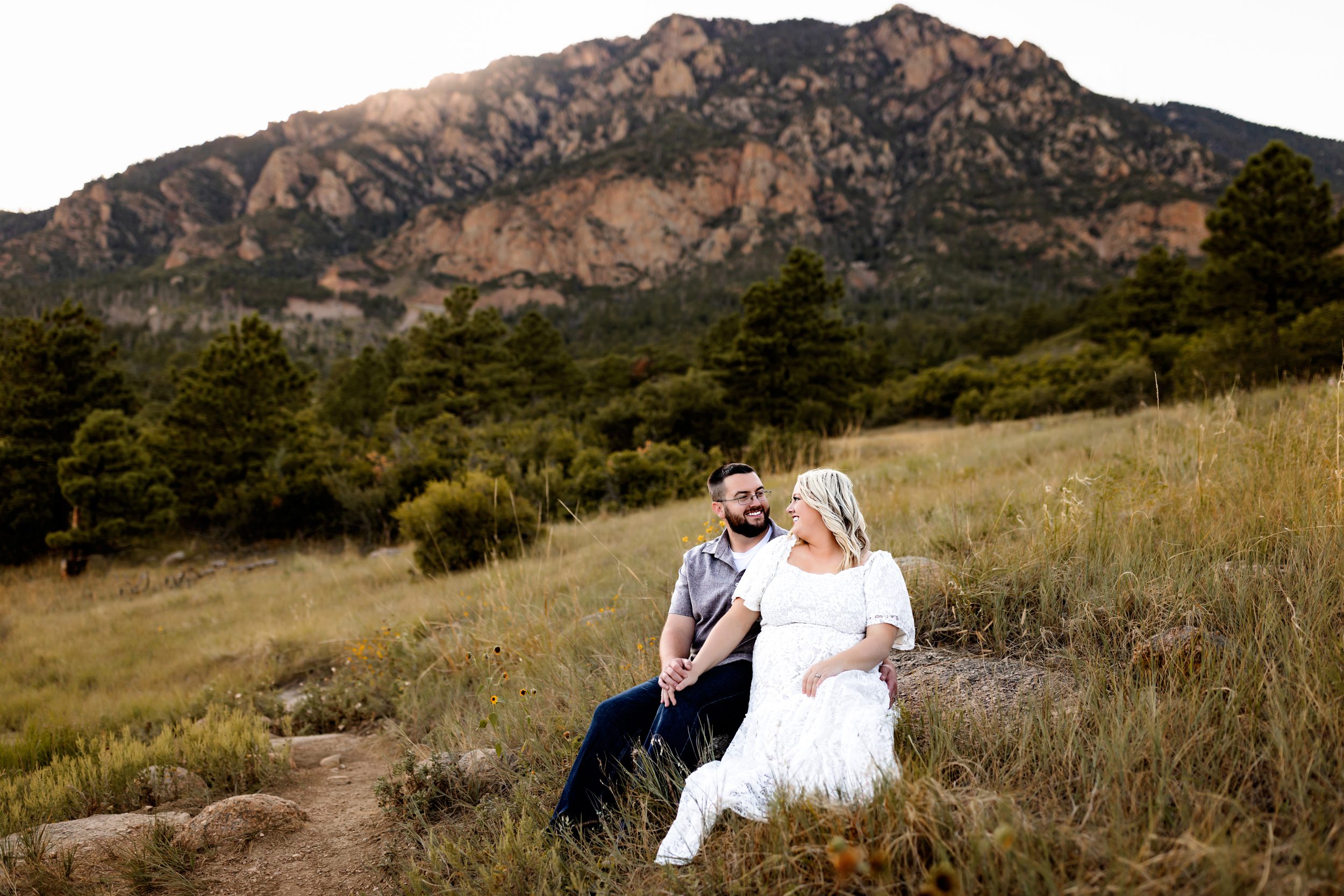 Anniversary Photos in Colorado Springs with a couple sitting on a rock, holding hands and smiling in front of a rugged mountain backdrop