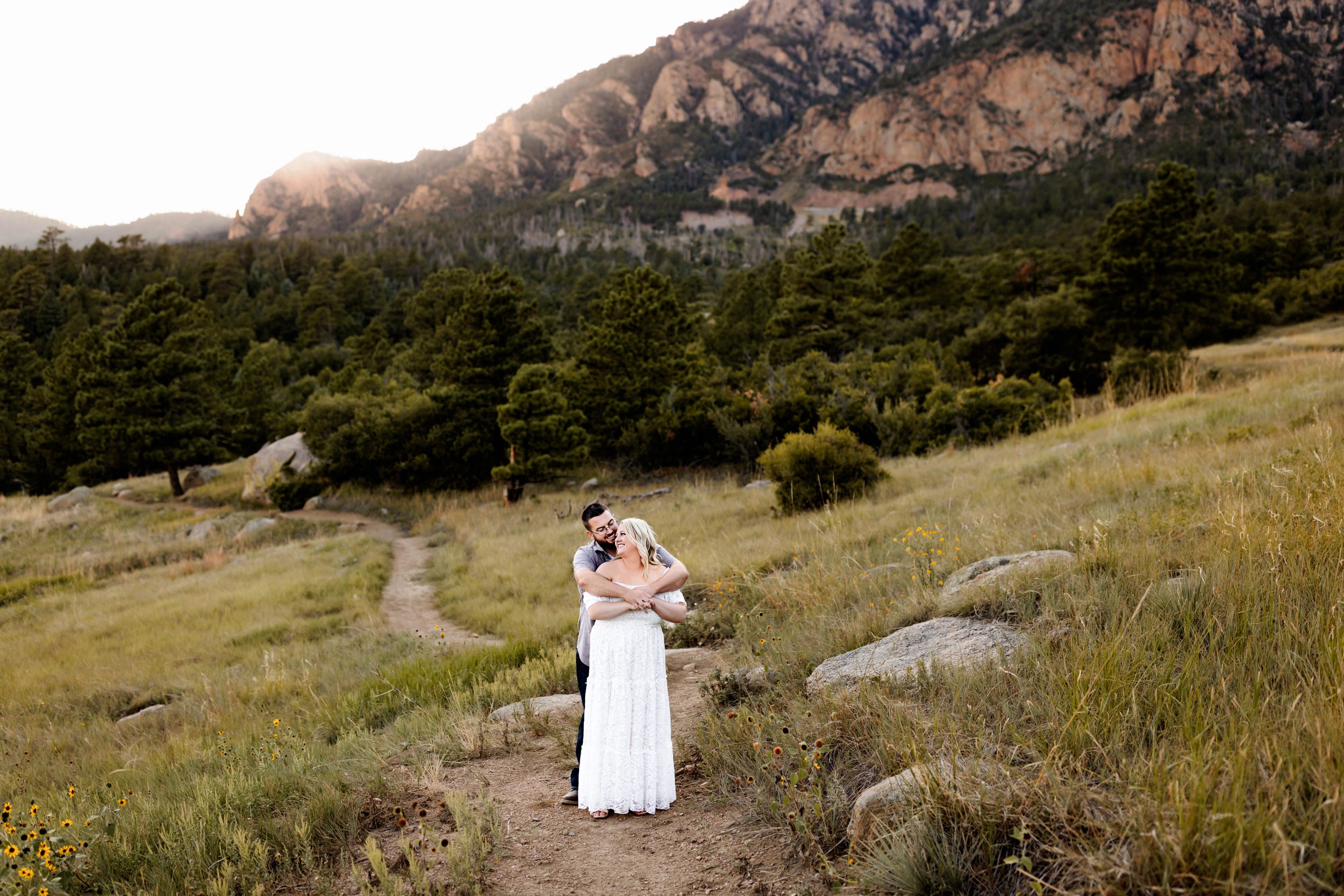 Anniversary Photos in Colorado Springs capturing a warm back hug as the couple gazes across the pine-covered hills