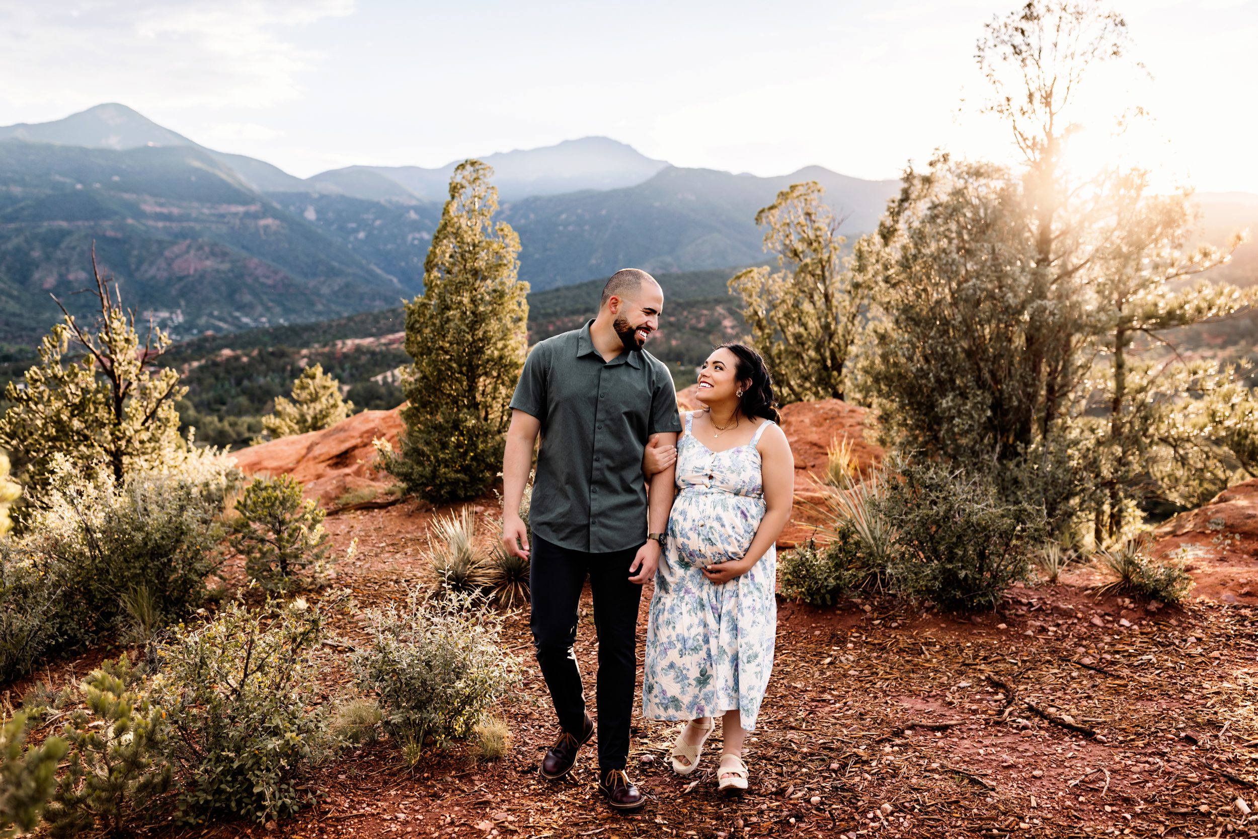 Couple walking through a forested trail during a Colorado Springs outdoor maternity session with mountain views