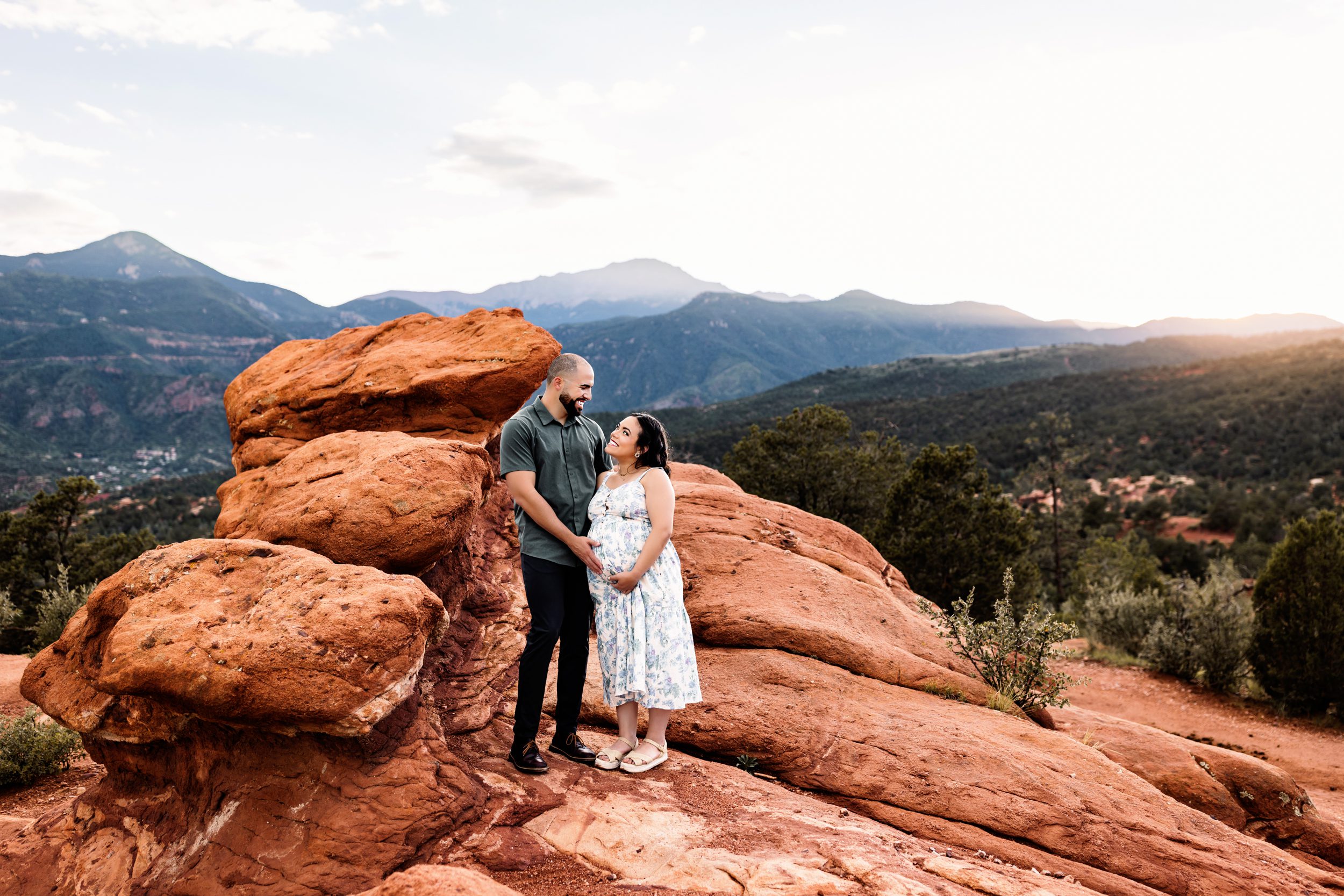 Couple smiling at each other while standing near unique rock formations and greenery