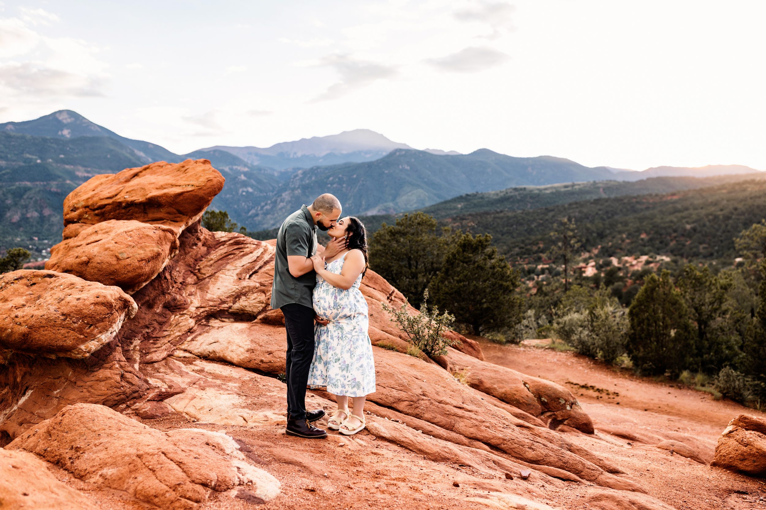 Couple sharing a kiss on red rocks at sunset during a Colorado Springs outdoor maternity session with mountain views