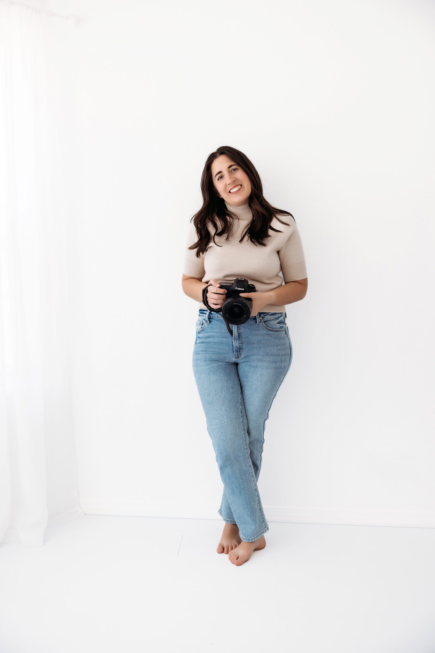 A photographer standing in a white room holding a camera