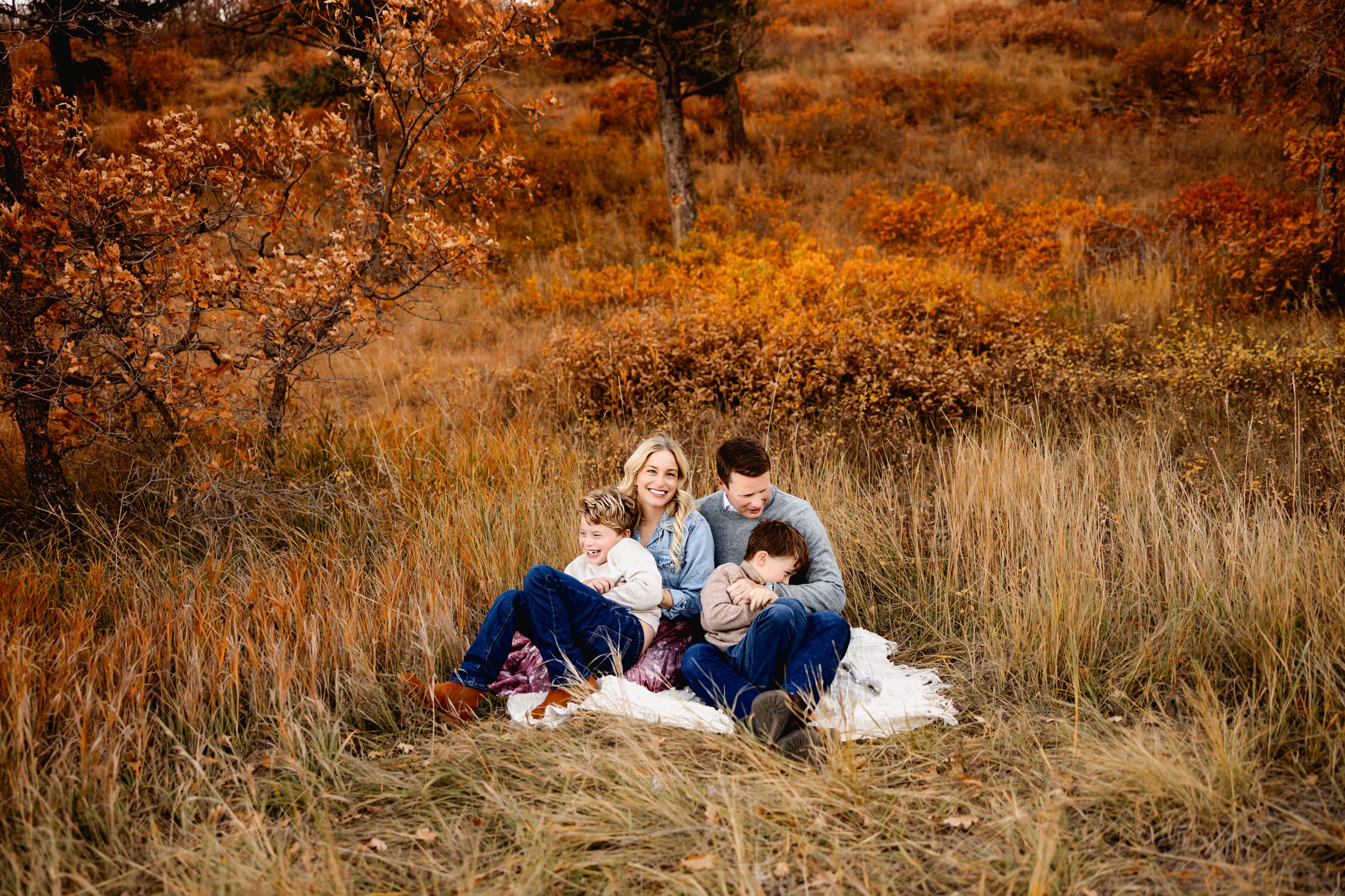 Family sitting close on a blanket in golden grass during their Fall Family Mini Session.