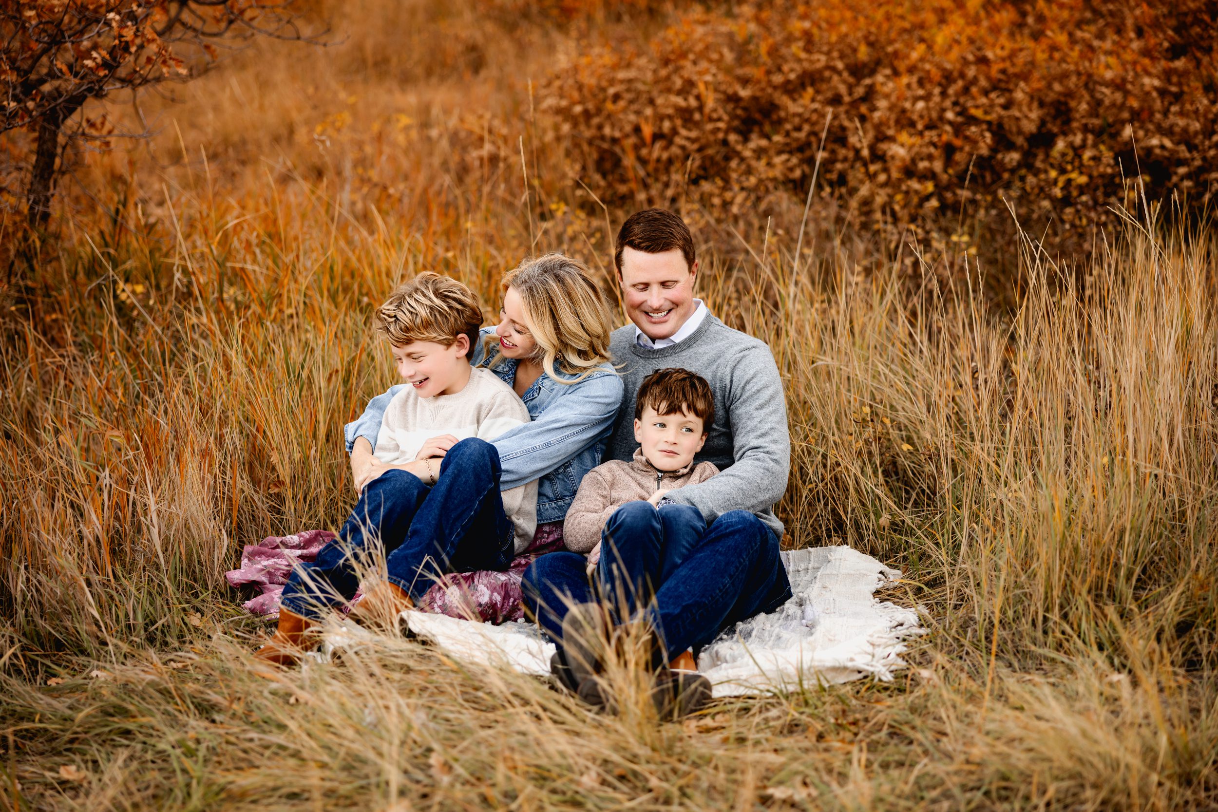 Family sitting close on a blanket in golden grass during their fall photo session