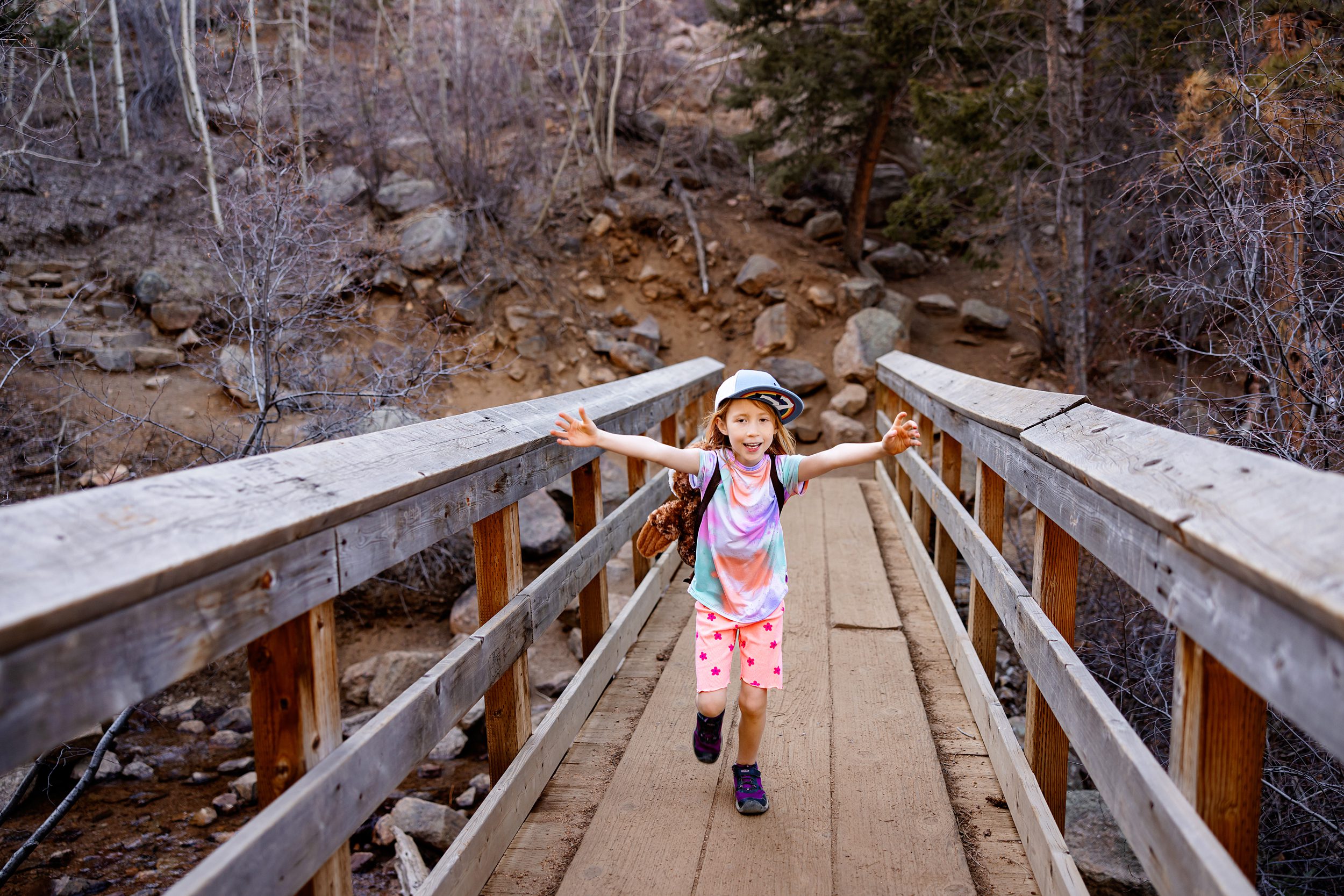 Child wearing an owl backpack jogging across a wooden bridge on a forest hike.