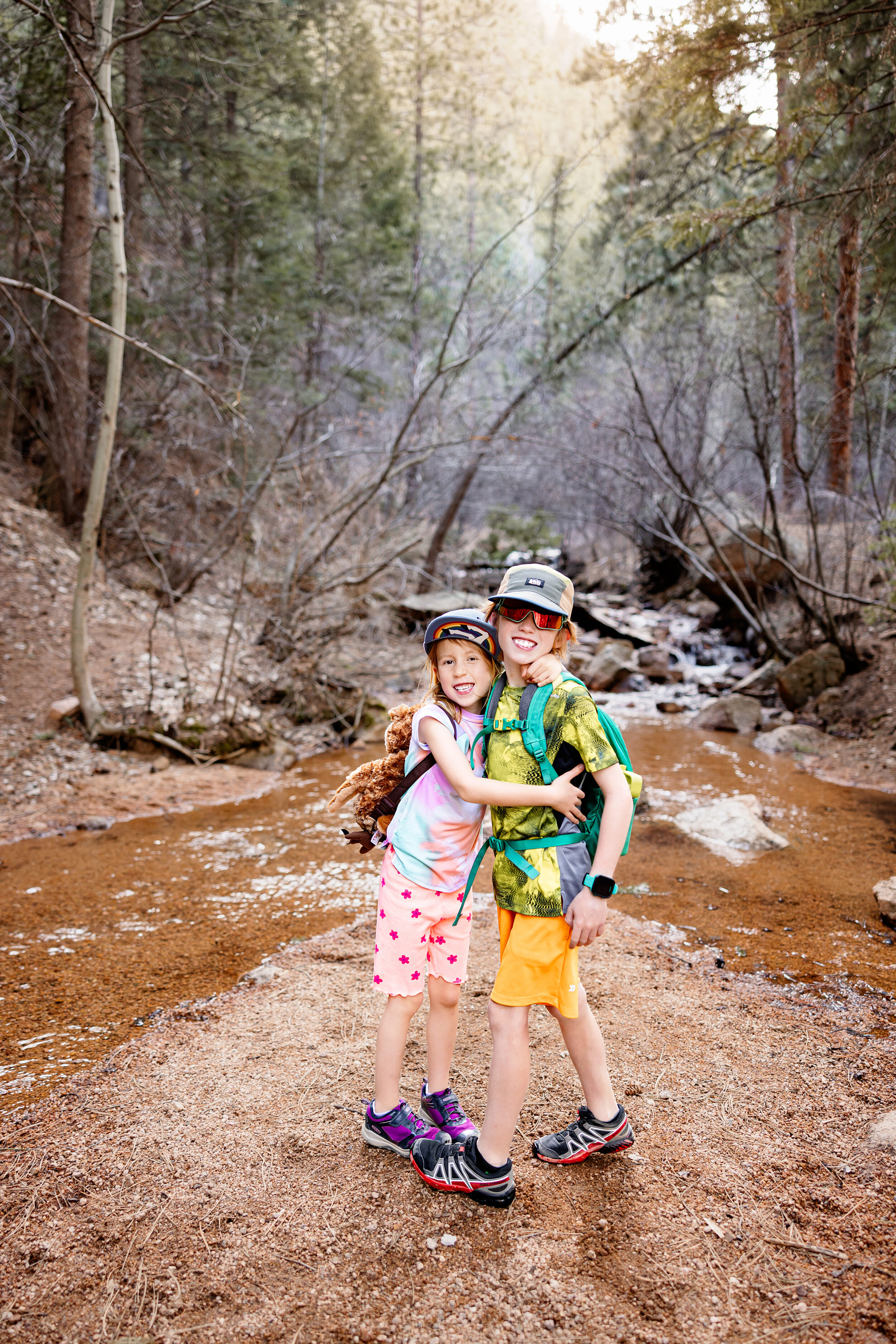 Two smiling kids hugging near a creek on one of the best family friendly hikes in Colorado Springs.