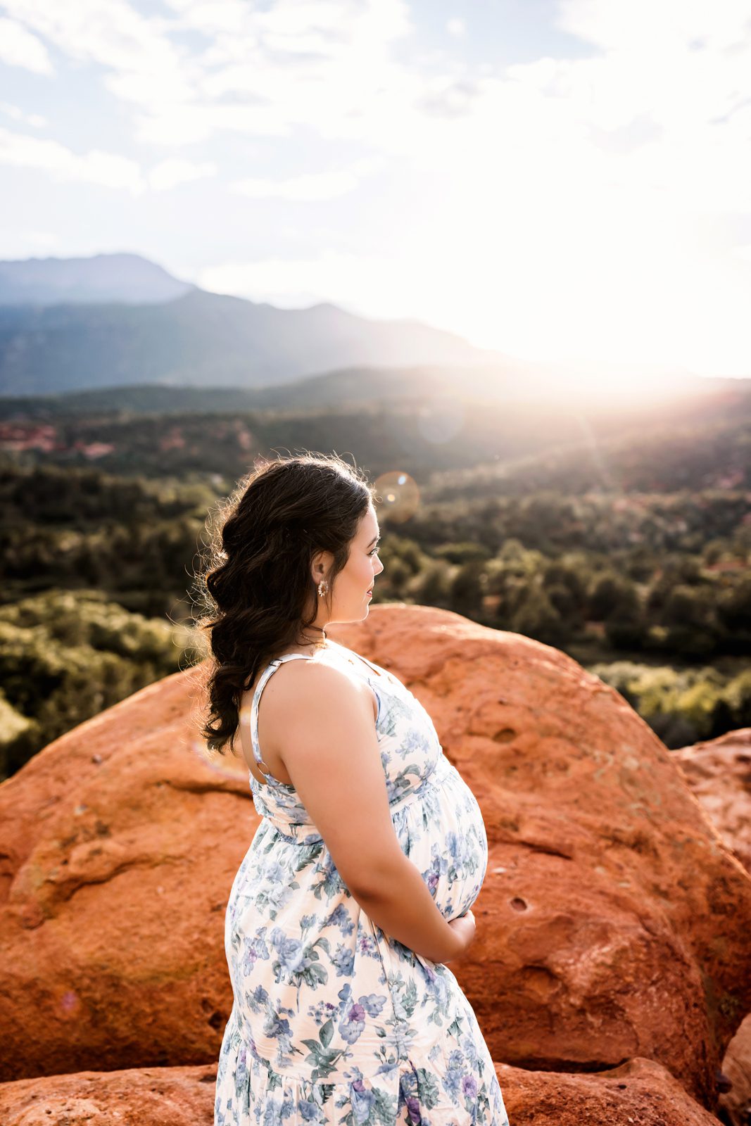 Side profile of mom-to-be holding her belly and looking at the sunlit mountain view