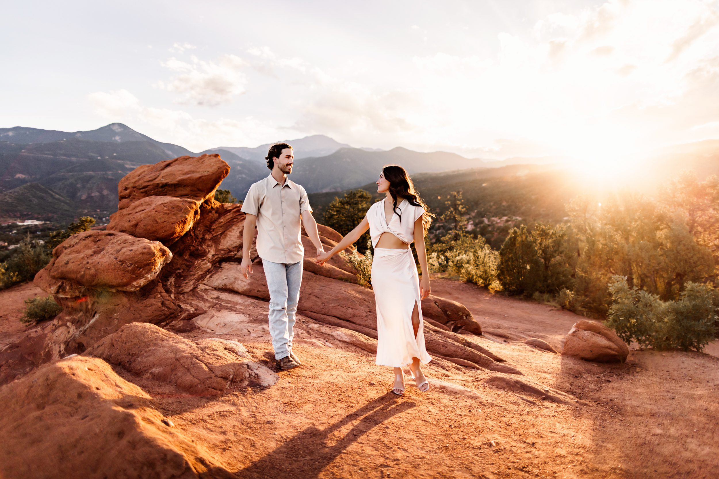 Golden hour walk during a couples session at Garden of the Gods with sun flares and rocky terrain.