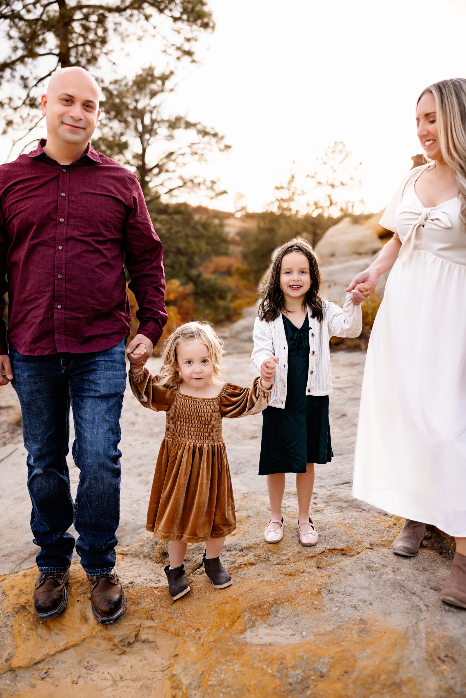 A young family holds hands with their daughters while walking across rocky terrain at their Fall Family Photo Session.