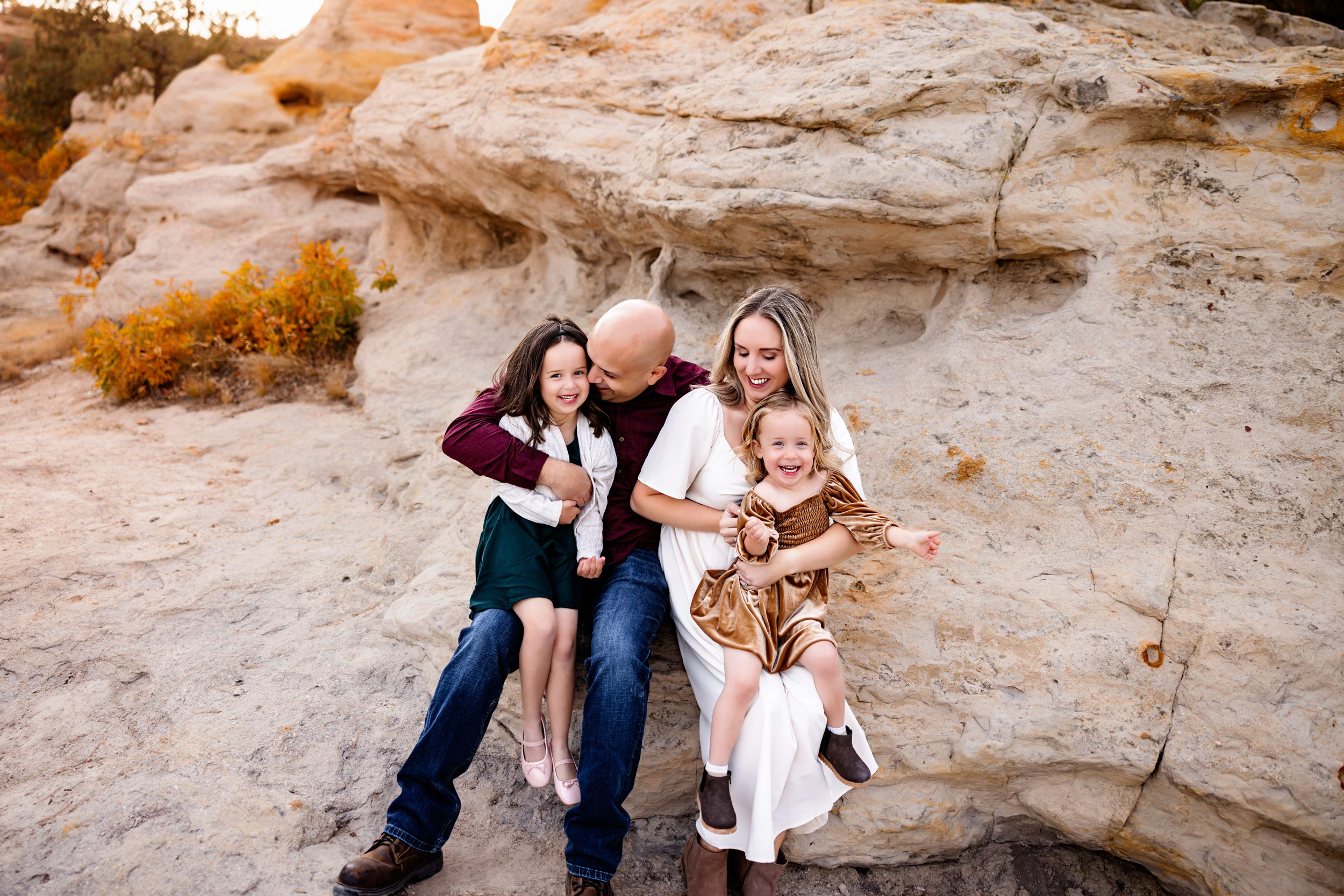 Parents tickle and laugh with their two daughters, capturing playful candid moments on a rocky trail.
