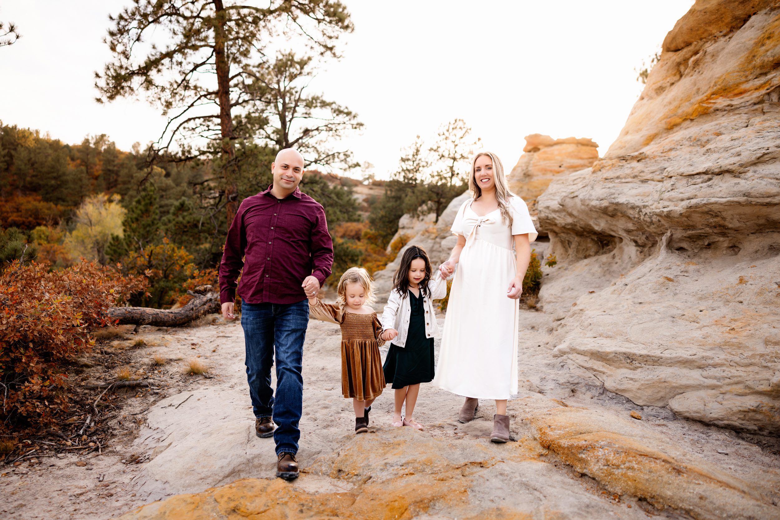 A family walks hand-in-hand down a trail lined with colorful fall foliage during their Fall Family Photo Session.
