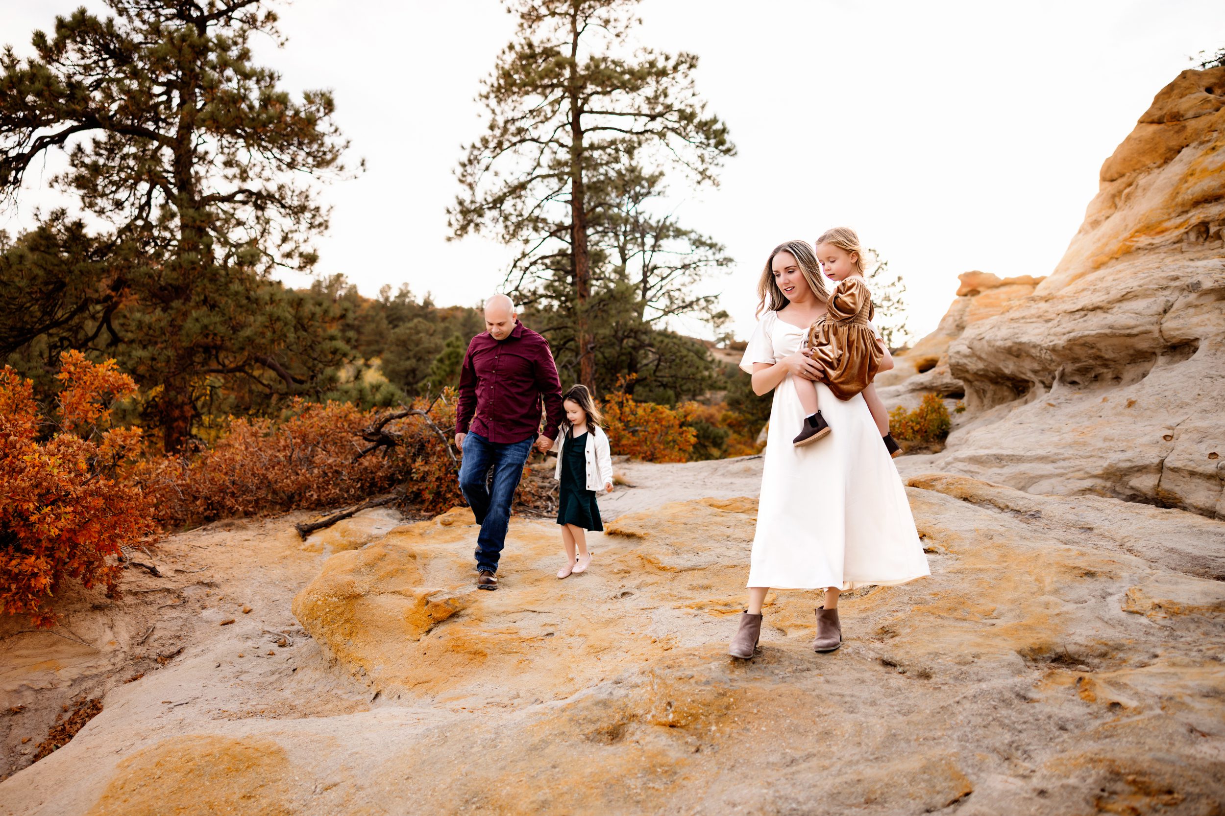 A family explores the rocks and trails at a scenic location with warm light and vibrant fall trees.