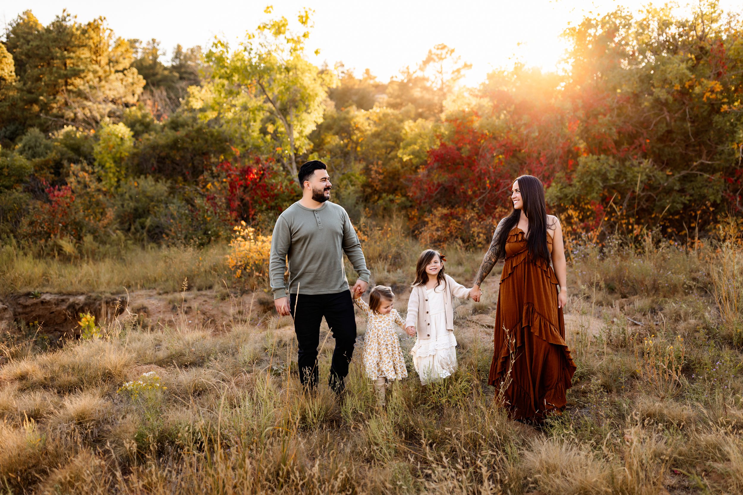 Joyful family walking through a field with fall foliage in Colorado Springs behind them.