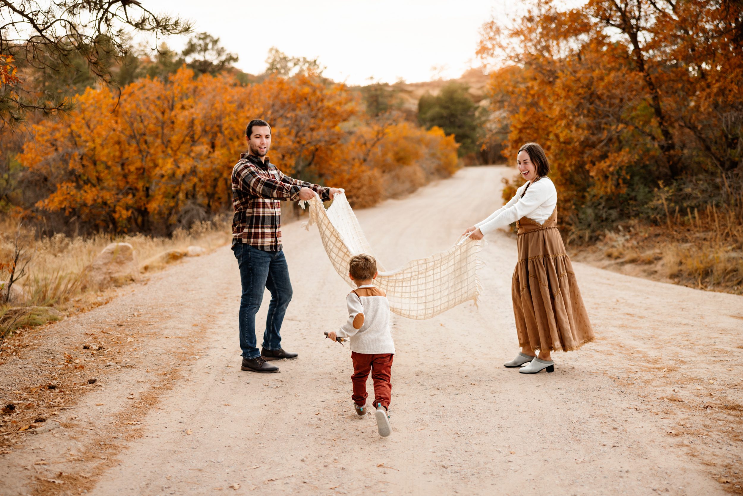 Family playing on a dirt road with vibrant orange trees, captured at one of the best fall photo locations in Colorado Springs.