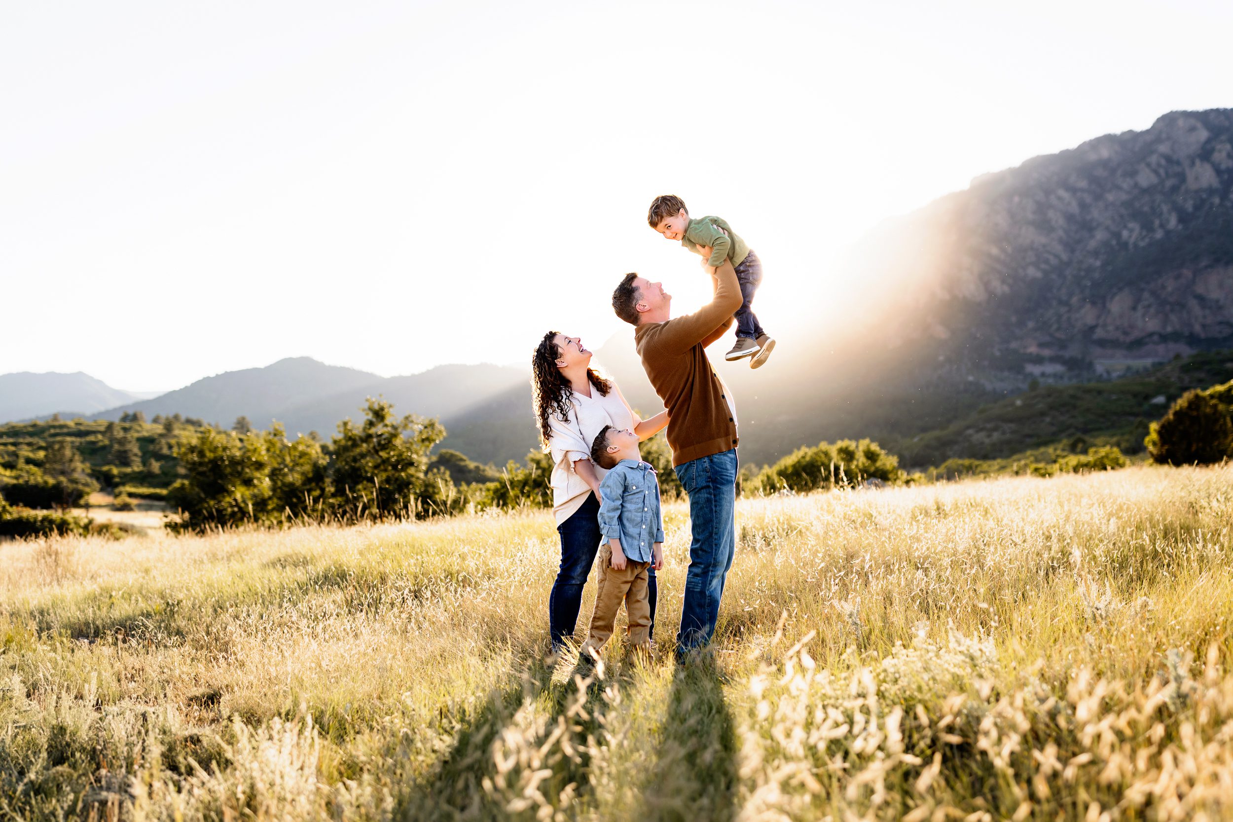 Parents lifting their child into the air with mountain views and golden light during a playful family photo session.
