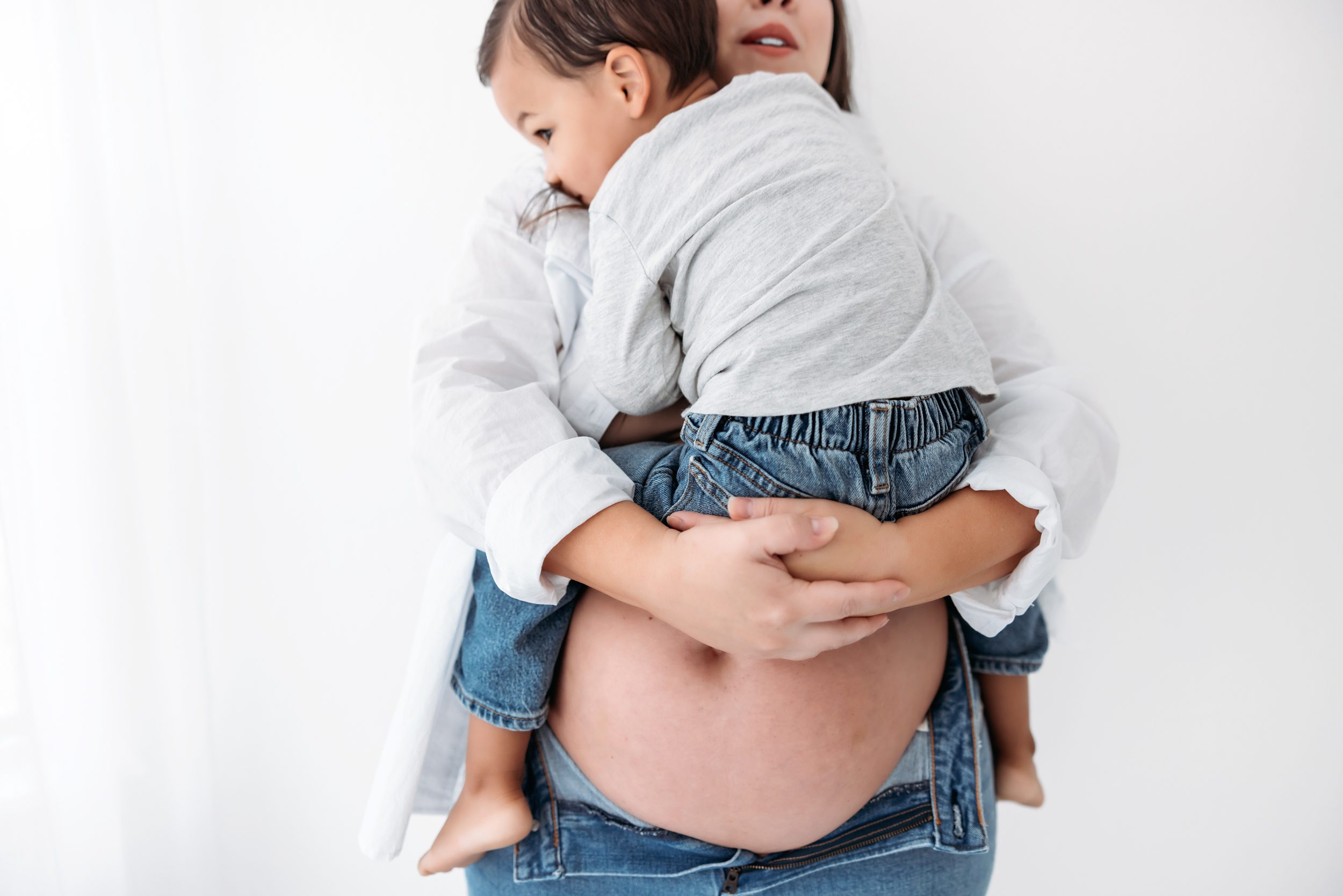 A pregnant mom holding her toddler while he gives her a hug all while showing off her baby bump