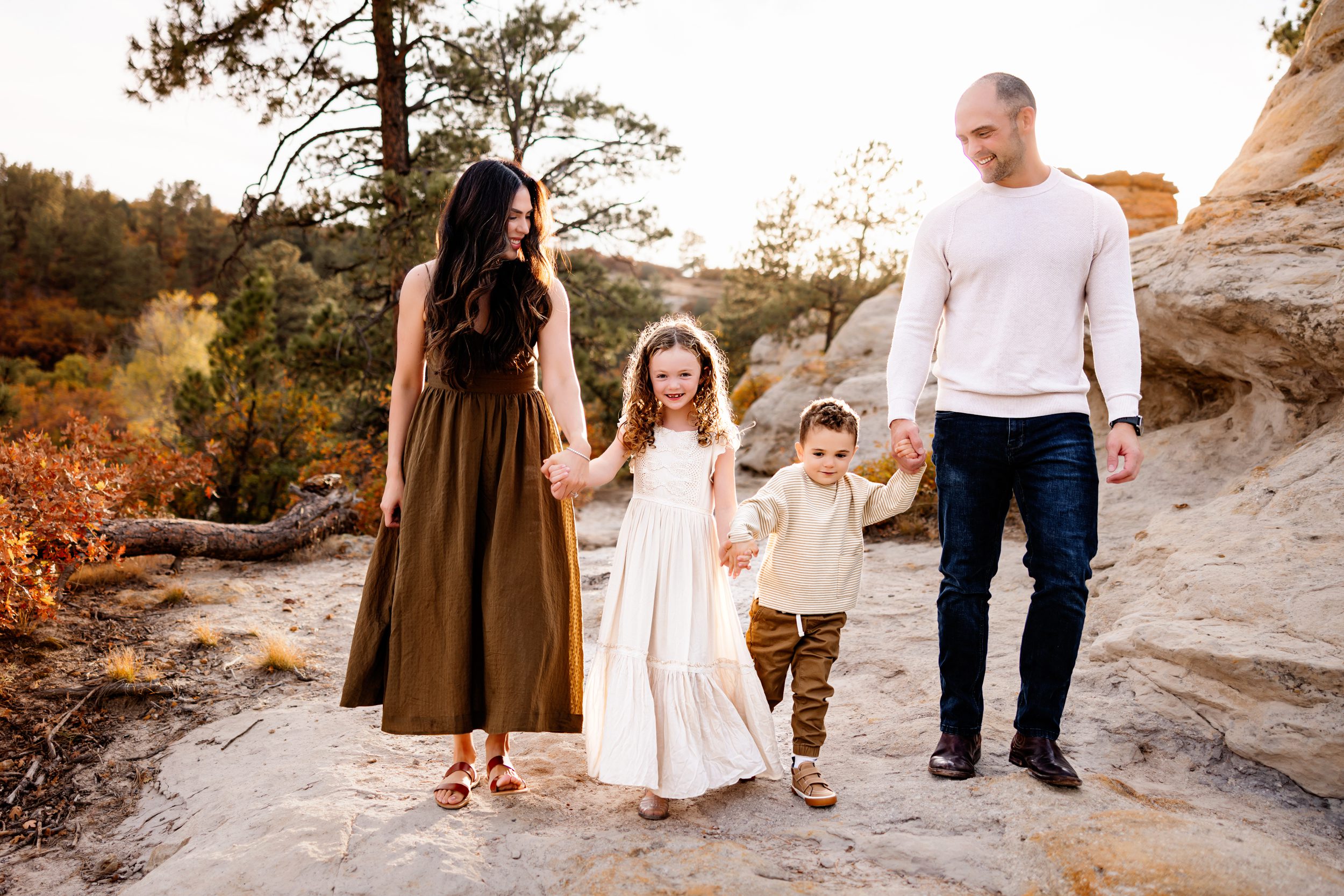 A family of four walks hand-in-hand during their Colorado Springs Fall Mini Session, surrounded by warm autumn colors and rocky scenery.