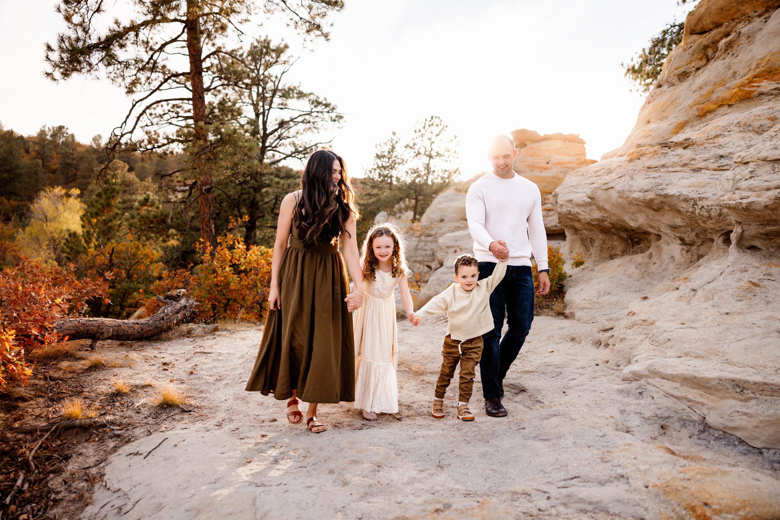 A happy family walks together down a sunlit trail, holding hands and laughing as golden light shines through the autumn trees.