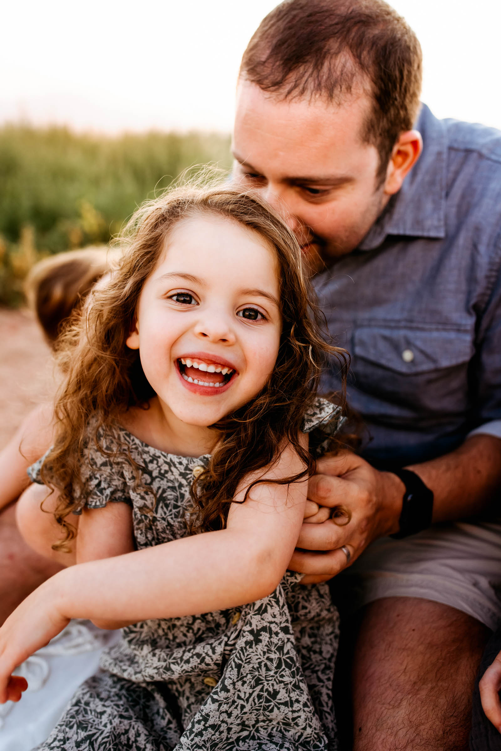 Father affectionately smiling behind his young daughter, who beams happily toward the camera.