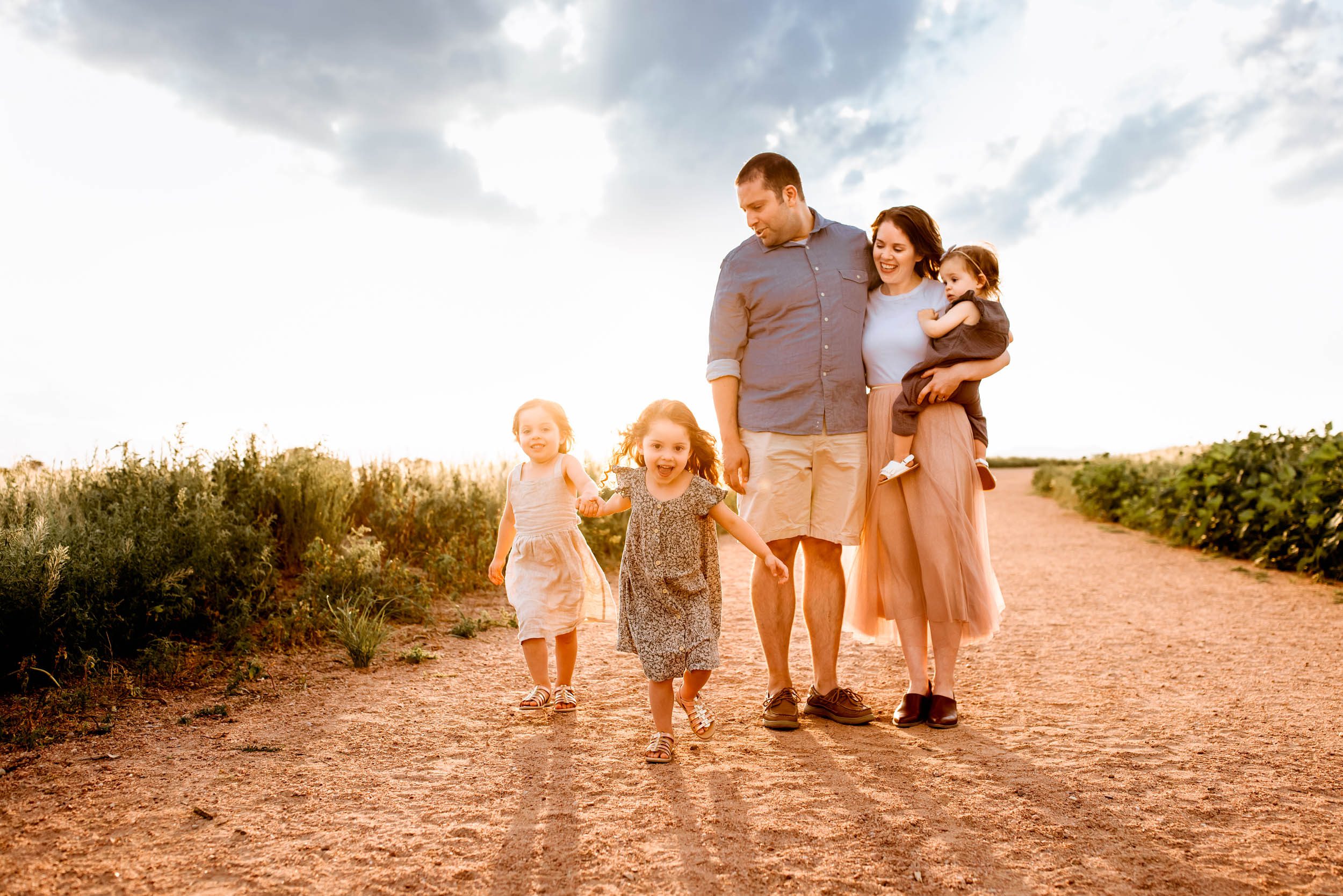Joyful family walking and playing together along a sunlit path, with two young girls running ahead excitedly.