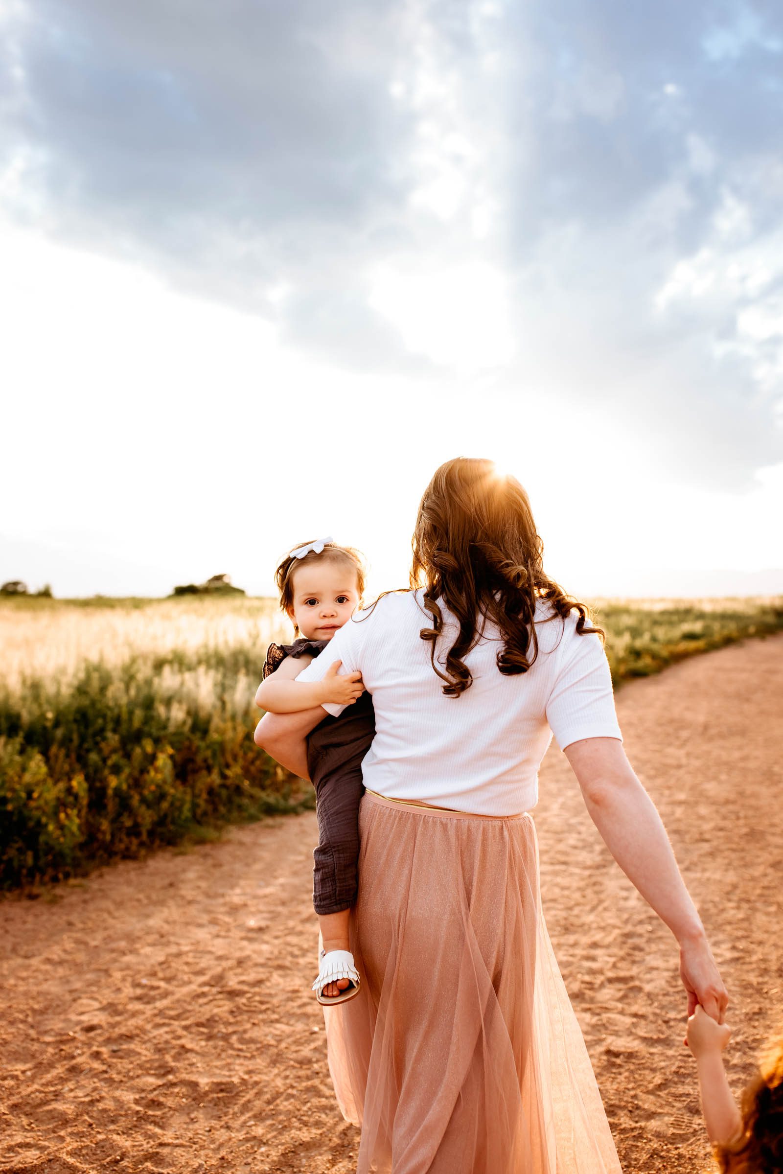 Mother holding her young child as they walk through warm sunlight during their Colorado Springs Summer Session.